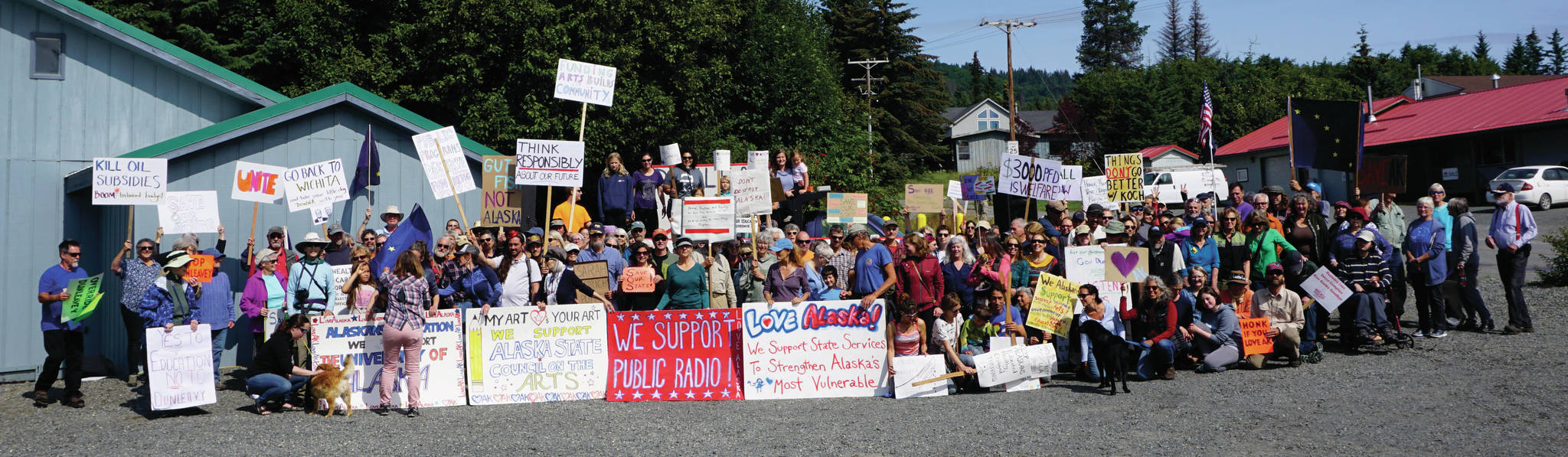 Demonstrators line up for a group photo on Sunday, July 28, 2019, outside the Legislative Information Office after a rally against Gov. Mike Dunleavy’s budget cuts in Homer, Alaska. (Photo by Michael Armstrong/Homer News)