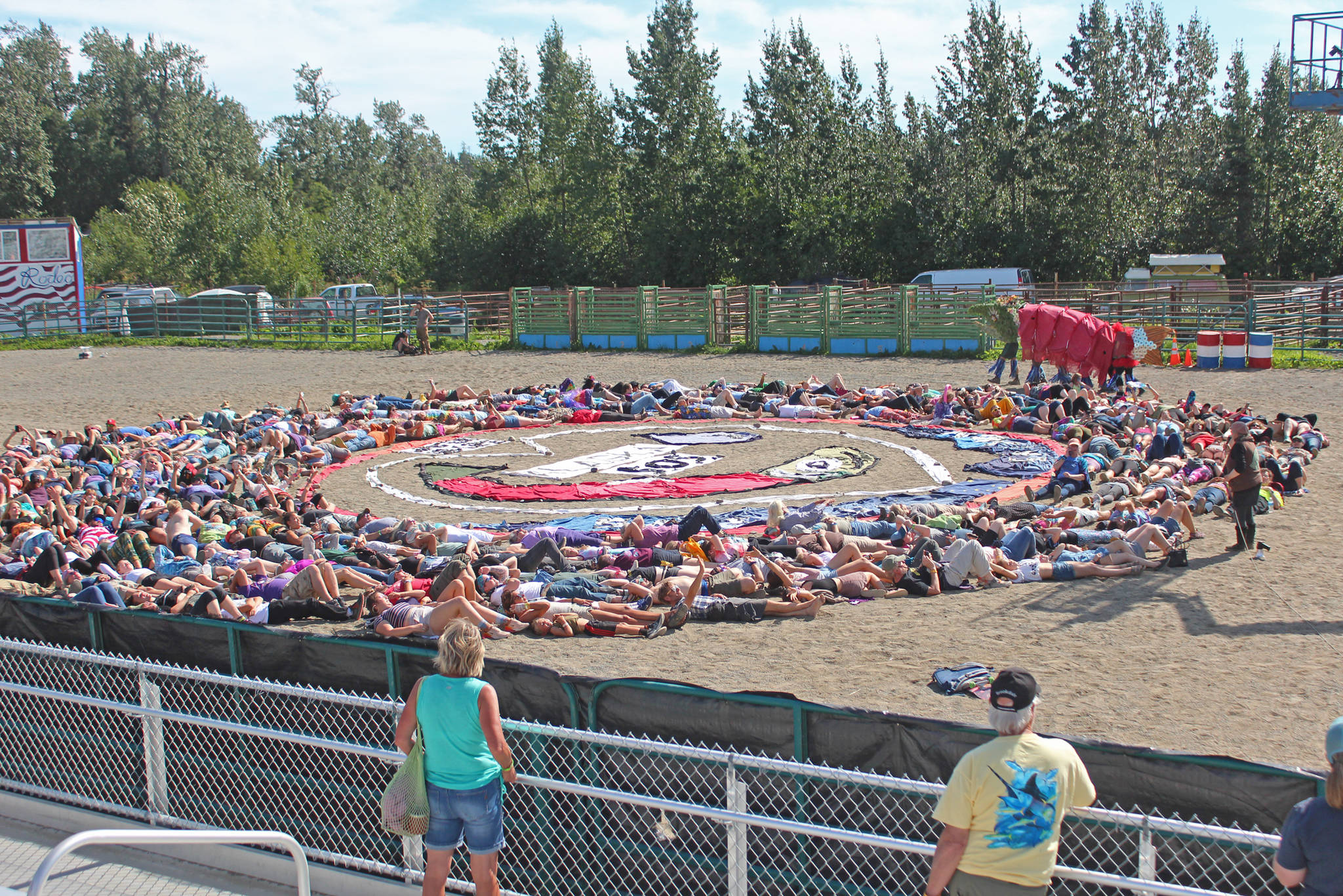Festival goers prepare to participate in the annual art installation by Homer artist and activist Mavis Muller on Saturday, Aug. 3, 2019 at Salmonfest in Ninilchik, Alaska. Each year, Muller designs an image having to do with salmon and water and makes it out of large pieces of cloth on the rodeo grounds at the Ninilchik Fairgrounds. People attending the festival then surround the image for the final touch while a photo is taken from the air. (Photo by Megan Pacer/Homer News)