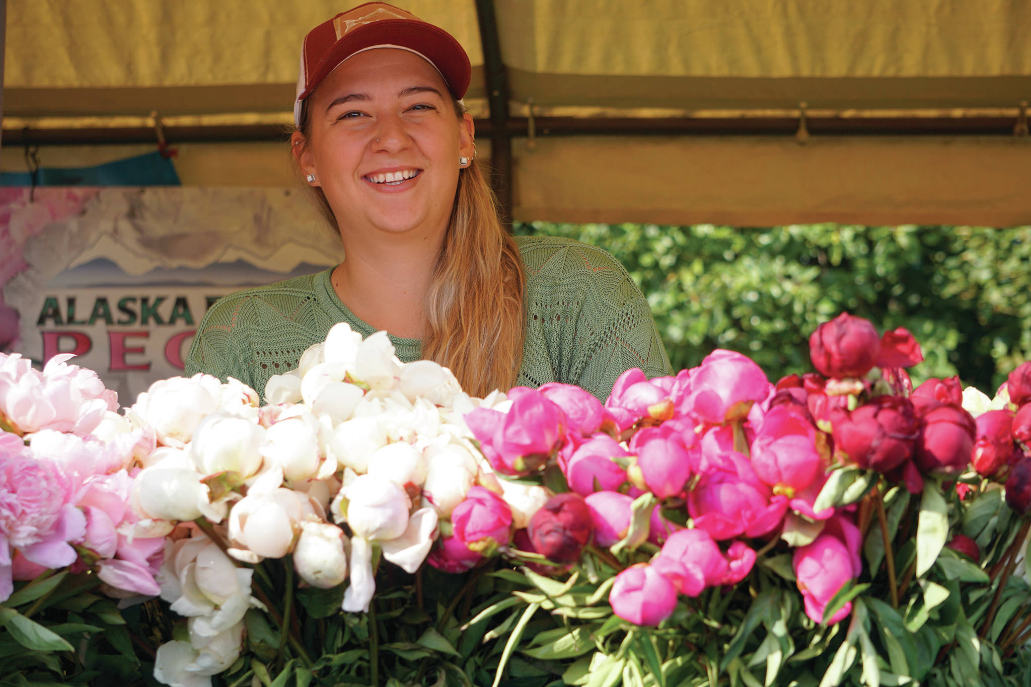 Genevieve Tymrak poses for a photo behind fresh-cut peonies on Saturday, Aug. 10, 2019, at the Alaska Perfect Peonies booth at the Homer Farmers Market in Homer, Alaska. (Photo by Michael Armstrong/Homer News)