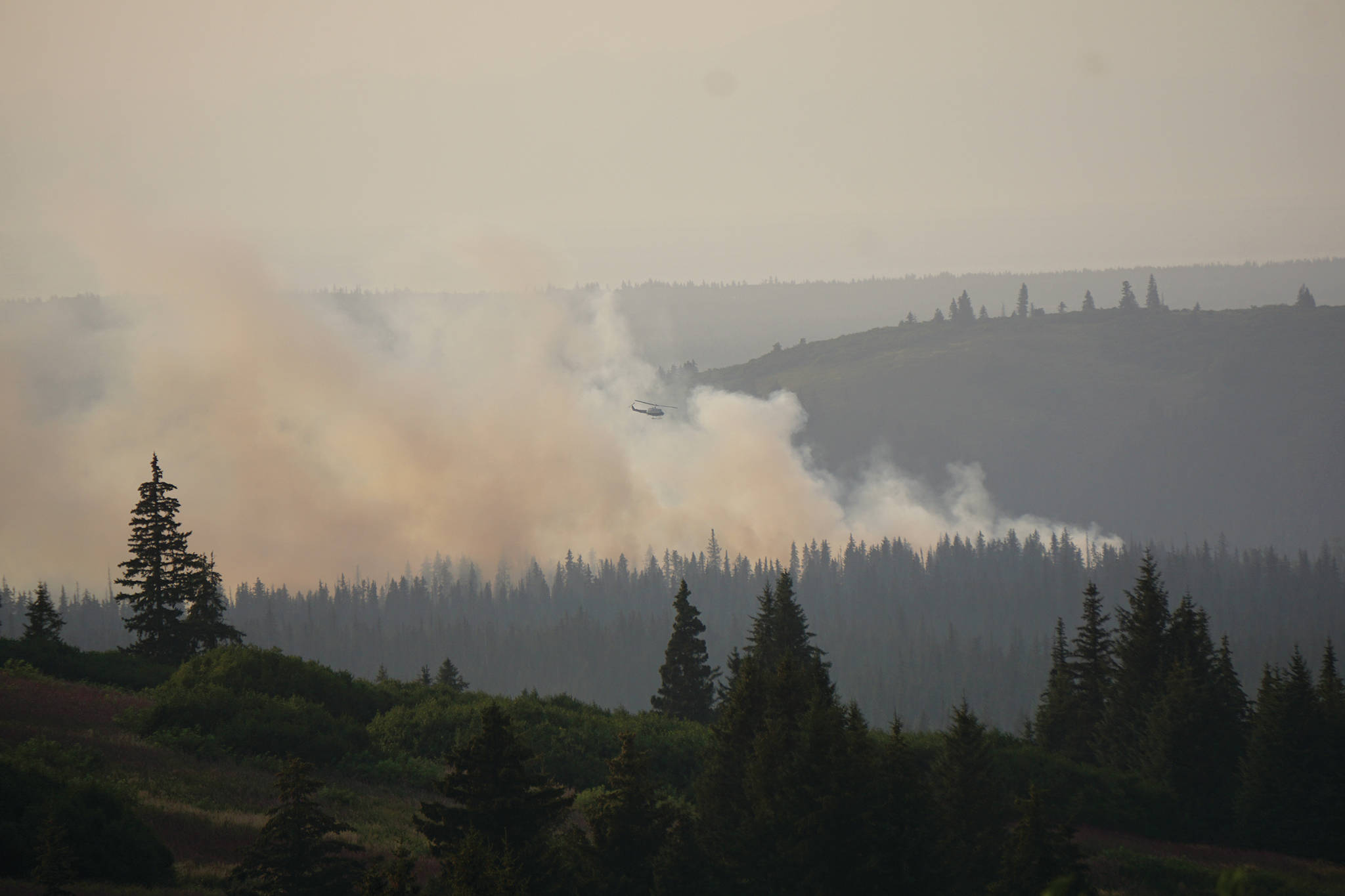 A helicopter flies over the North Fork fire as it burns near the south end of the North Fork Road on Sunday evening, Aug. 18, 2019, near Homer, Alaska, as seen from Diamond Ridge Road. (Photo by Michael Armstrong/Homer News)