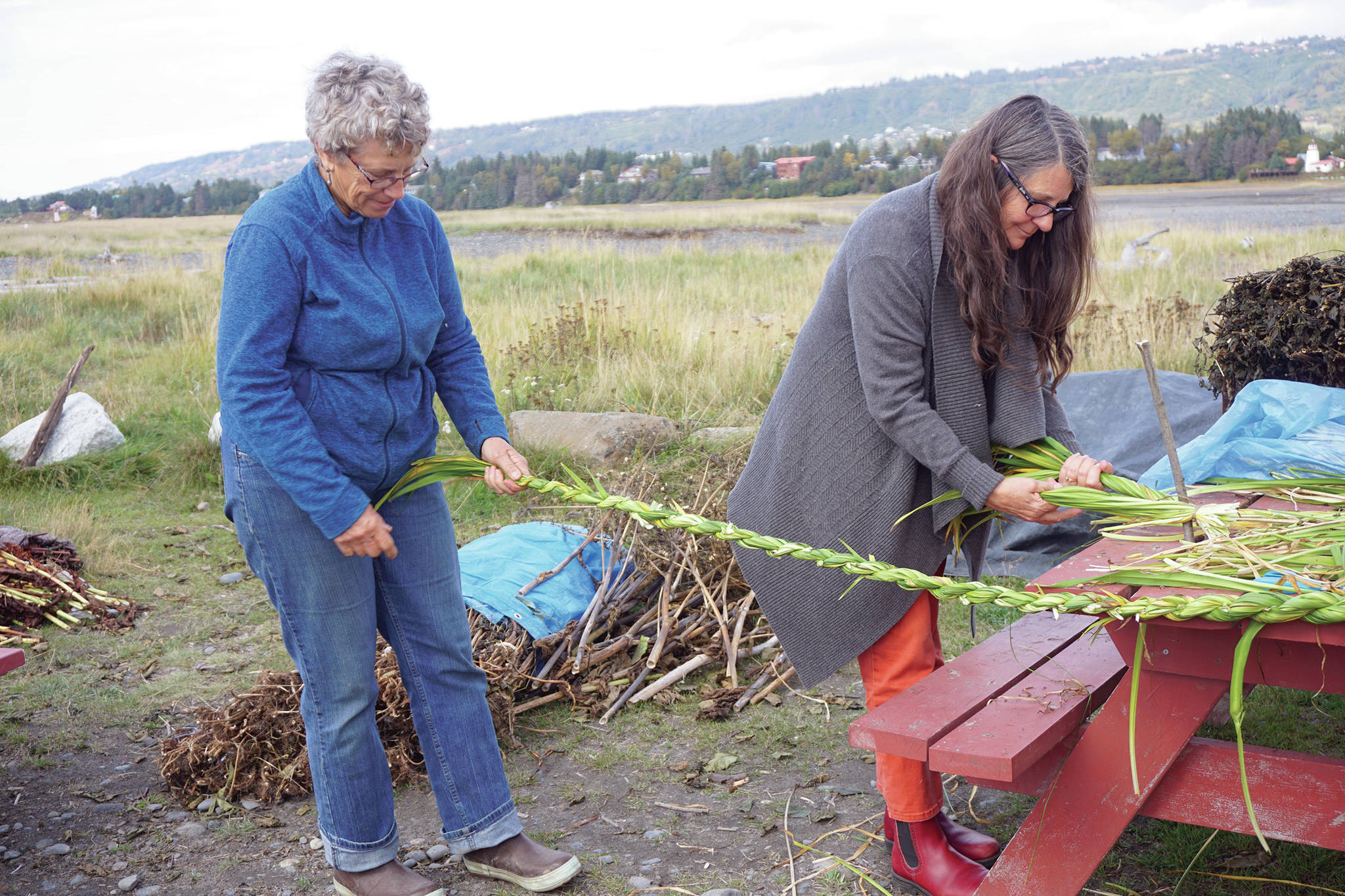Peggy Gavillot, left, and Lora Wilke, right weave leaves for the 16th annual Burning Basket, Radiate, on Tuesday, Sept. 10, 2019, at Mariner Park on the Homer Spit in Homer, Alaska. (Photo by Michael Armstrong/Homer News)