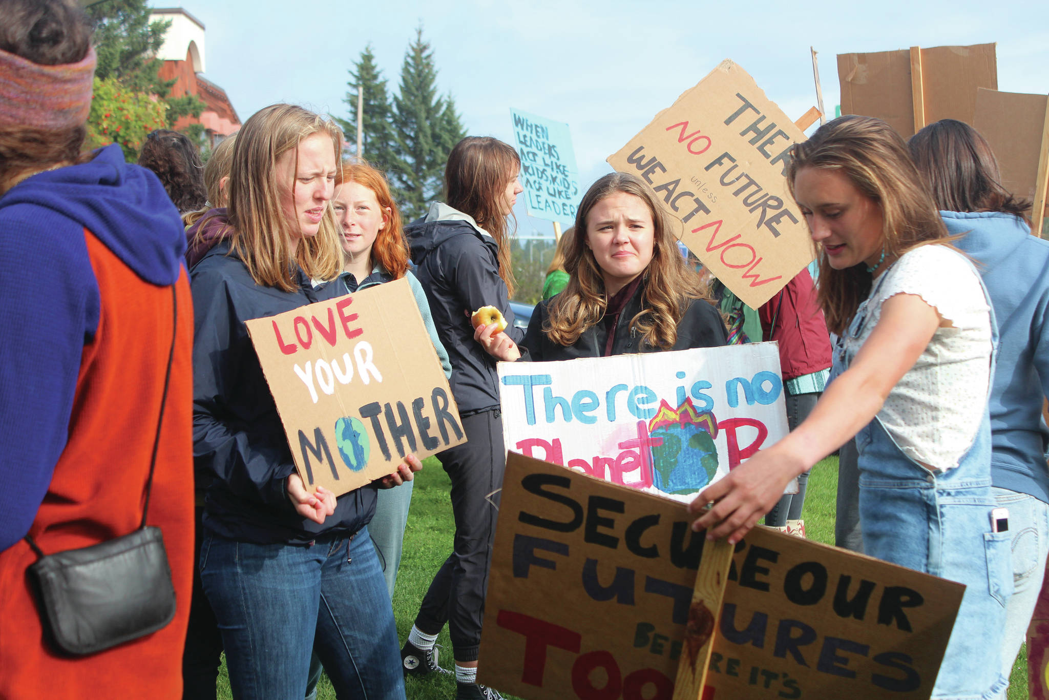 Homer High School students compare signs at the start of the Homer Youth Climate Strike on Friday, Sept. 20, 2019 at Wisdom, Knowledge, Faith and Love Park in Homer, Alaska. Students left school before their sixth period to hold the rally in the park and were joined by community members. (Photo by Megan Pacer/Homer News)