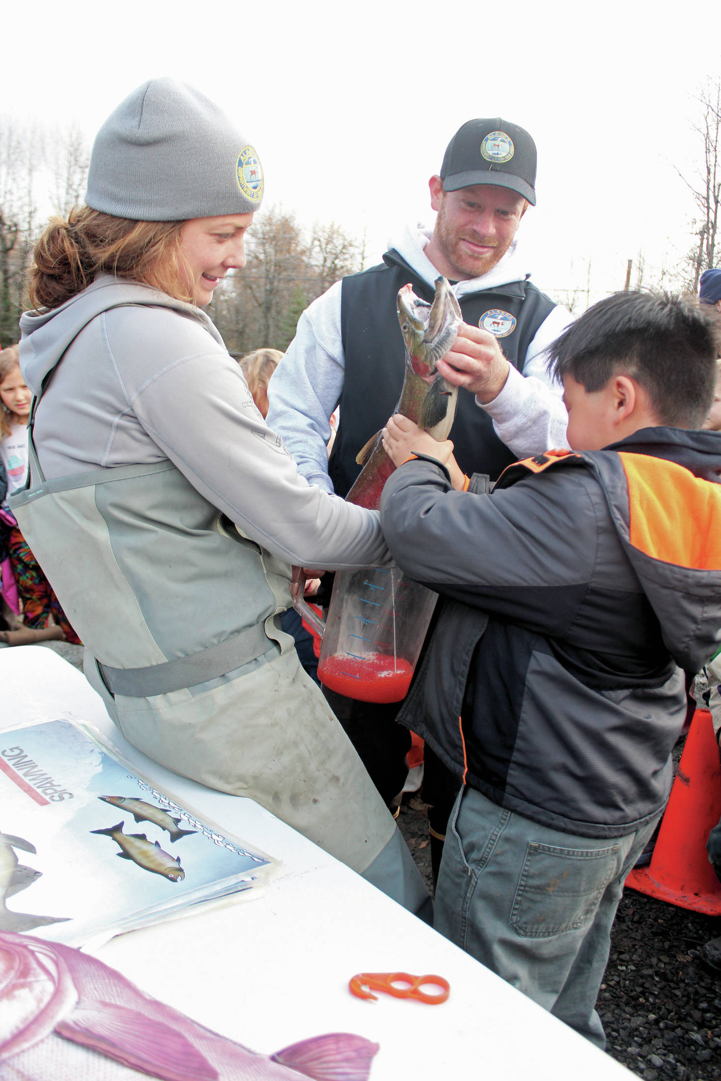 Alaska Department of Fish and Game biologists Holly Dickson (left) and Andrew Waldo (center) help Chapman School second grader Khian Tangnon (right) empty the milt from a male salmon into a pitcher of salmon eggs during the annual egg take event at the Anchor River on Thursday, Oct. 10, 2019 in Anchor Point, Alaska. The egg take is the first phase in the Salmon in the Classroom project. (Photo by Megan Pacer/Homer News)