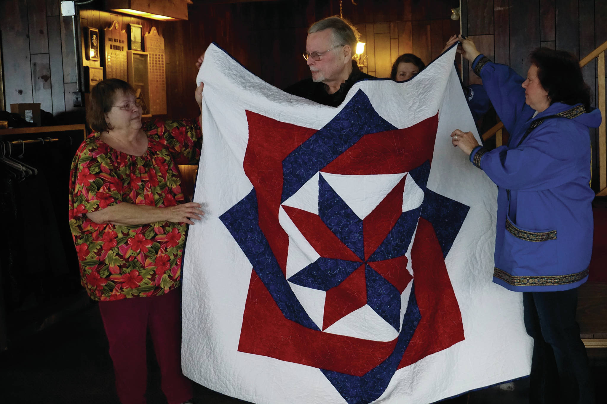 Nick Varney, center, stands behid a Quilt of Valor presented to him at the Veterans Day lunch held at the Elks Lodge on Nov. 11, 2019, in Homer, Alaska. To his right is Linda Wagner, who pieced the quit. Varney served in the U.S. Air Force and the Alaska Air National Guard. (Photo by Michael Armstrong/Homer News)