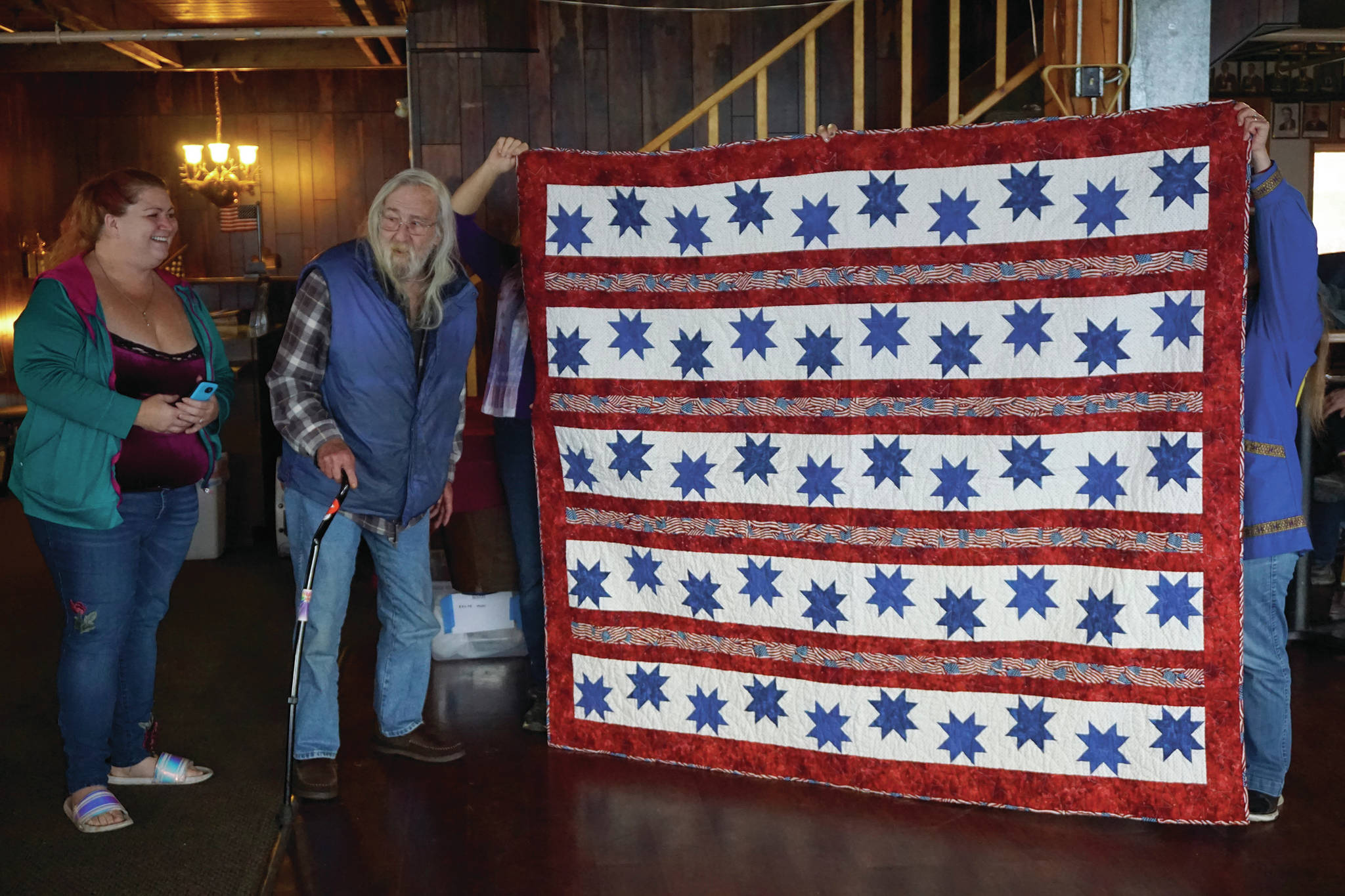 John Benya stands by a Quilt of Valor presented to him at the Veterans Day lunch held at the Elks Lodge on Nov. 11, 2019, in Homer, Alaska. To his right is his daughter, Joy Davis. Benya served in the U.S. Army from 1965-66, including a tour in Vietnam, where he was wounded in action. (Photo by Michael Armstrong/Homer News)