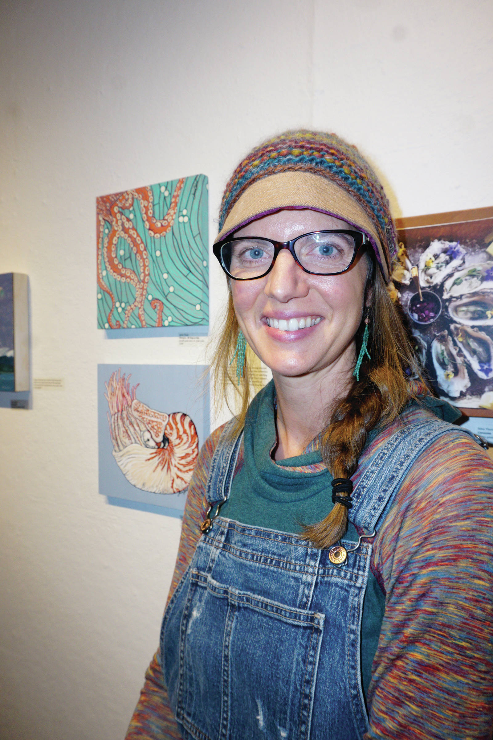 Jamie Cloud poses next to her paintings, some of the works of art in the 10x10 show at Bunnell Street Arts Center that opened on Nov. 8, 2019, in Homer, Alaska. (Photo by Michael Armstrong/Homer News)