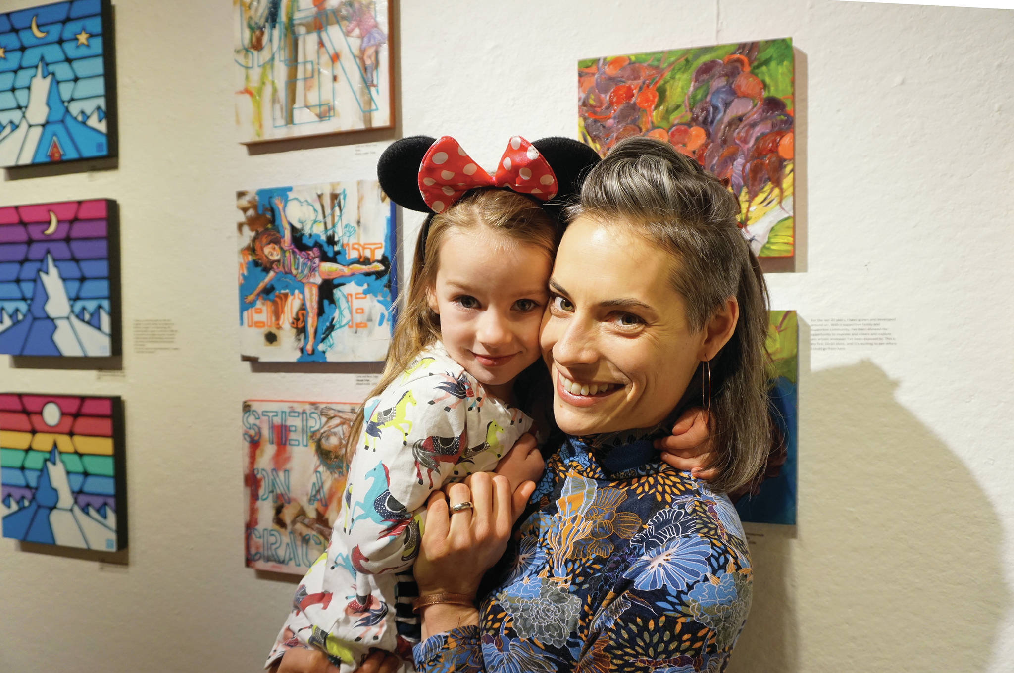 Carla Klinker Cope and her daughter, Nova, pose next to their paintings at left at the Nov, 8, 2019, opening of the 10x10 show at Bunnell Street Arts Center. Nova painted the background elements to the paintings and her mother added to that. (Photo by Michael Armstrong/Homer News)