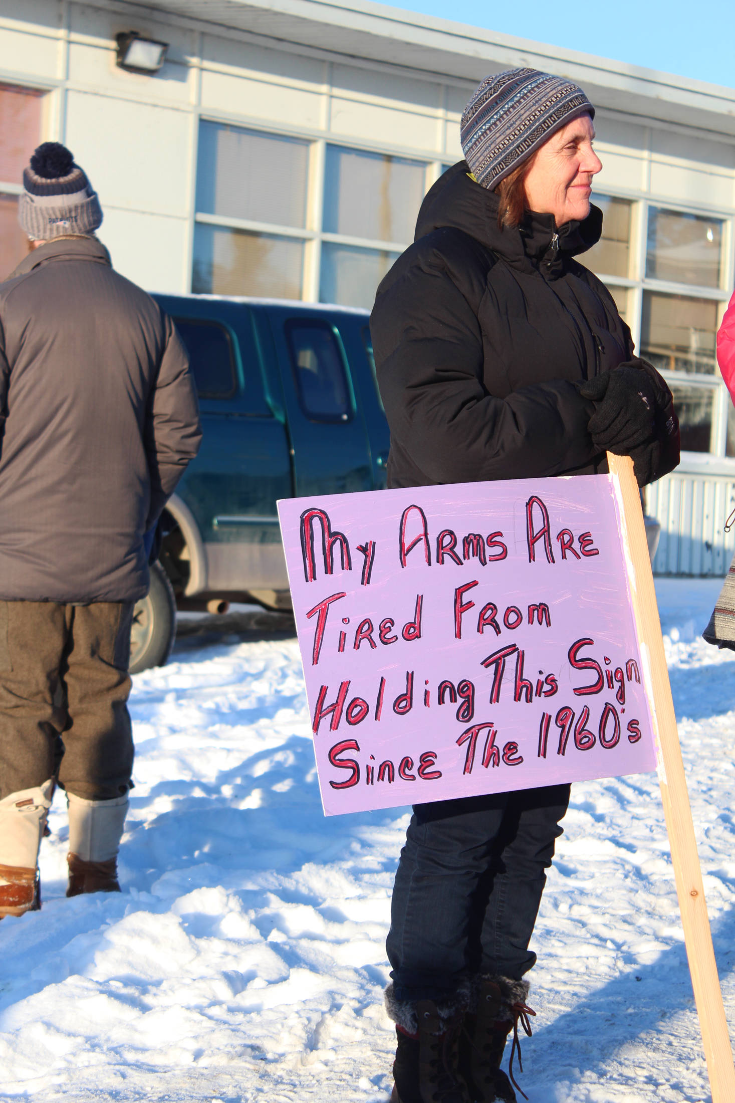 A woman holds a sign that reads “My arms are tired from holding this sign since the 1960s” before the fourth Women’s March on Homer on Saturday, Jan. 18, 2020 in Homer, Alaska. About 300 community members gathered outside the Homer Education and Recreation Complex before marching down Pioneer Avenue to WKFL Park. (Photo by Megan Pacer/Homer News)