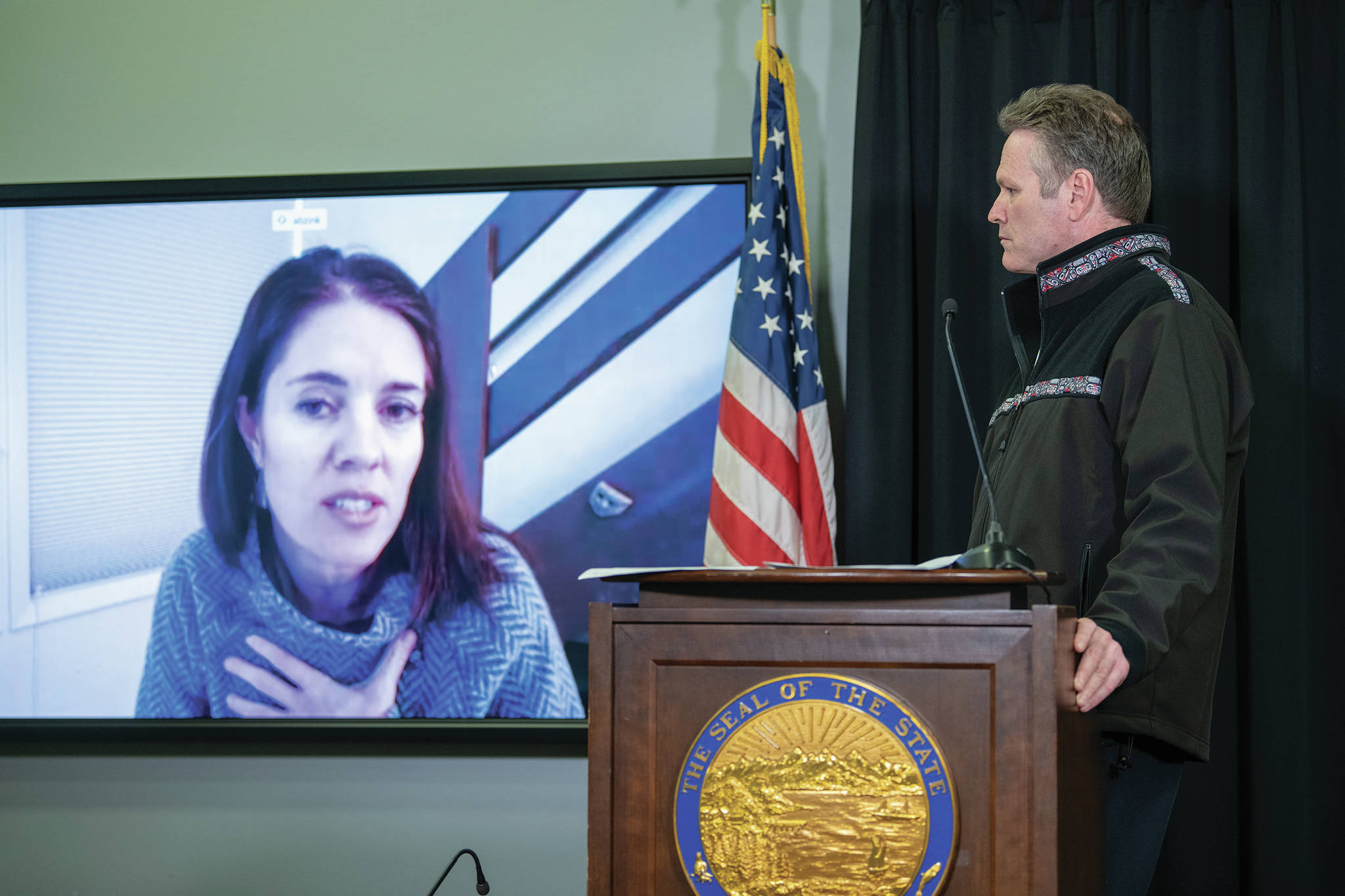 Alaska Chief Medical Officer Dr. Anne Zink, left, speaks by video in a press conference on April 6, 2020, in Juneau, Alaska, while Gov. Mike Dunleavy, right, listens. (Photo by Austin McDaniel, Alaska Governor’s Office)