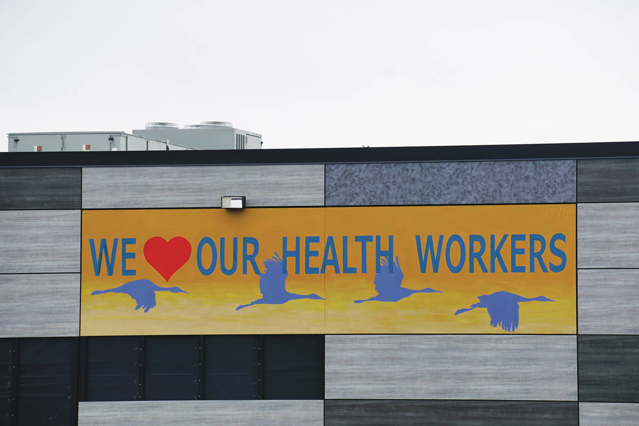 Artists David Pettibone and Austin Parkhill put up a temporary message appreciating health workers on the side of the new Homer Police Station facing Heath Street on Saturday, April 11, 2020, in Homer, Alaska. “It just seemed like a fitting thing to do, Pettibone said. “We all need these uplifting messages right now.” The artists received a 1%-for-art commission to install a larger mural featuring sandhill cranes in flight that will be installed later in May. (Photo by Michael Armstrong/Homer News)