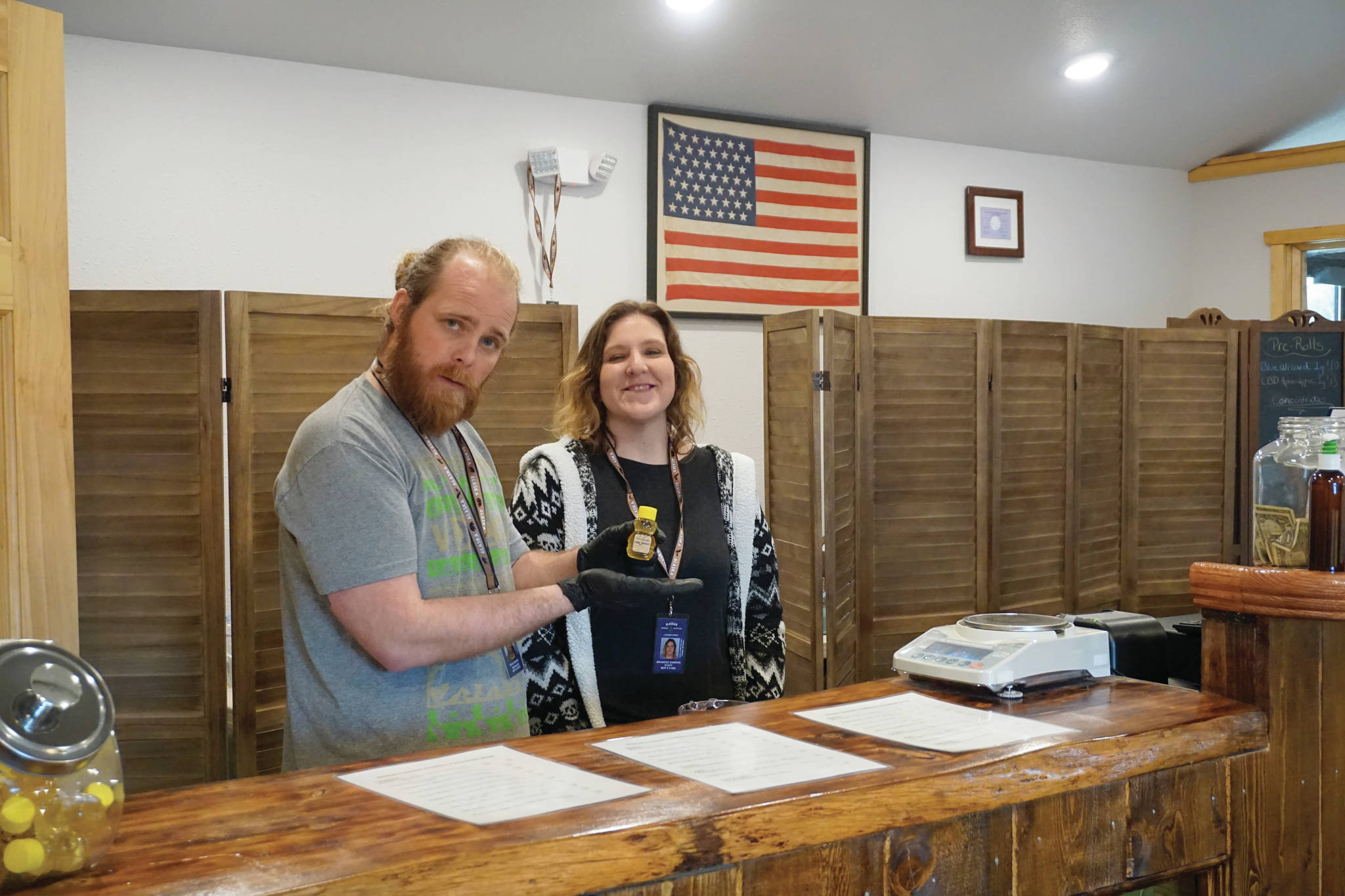 Micah Bear displays a bottle of CBD honey while manager Brandee Damore watches at the opening day of Alaskan Cannabis Outfitters, a new cannabis retail store. It’s is located right at Mile 168 Sterling Highway just before the road turns toward Baycrest Hill. The store opened on 4/20 — April 20, 2020 — in Homer, Alaska. Micah Bear’s brother, Ian Bear, is the licensed owner of the store founded by their father, Bill Bear, who died in December 2019. (Photo by Michael Armstrong/Homer News)                                Micah Bear displays a bottle of CBD honey while manager Brandee Damore watches at the opening day of Alaskan Cannabis Outfitters, a new cannabis retail store. It’s is located right at Mile 168 Sterling Highway just before the road turns toward Baycrest Hill. The store opened on 4/20 — April 20, 2020 — in Homer, Alaska. Micah Bear’s brother, Ian Bear, is the licensed owner of the store founded by their father, Bill Bear, who died in December 2019. (Photo by Michael Armstrong/Homer News)