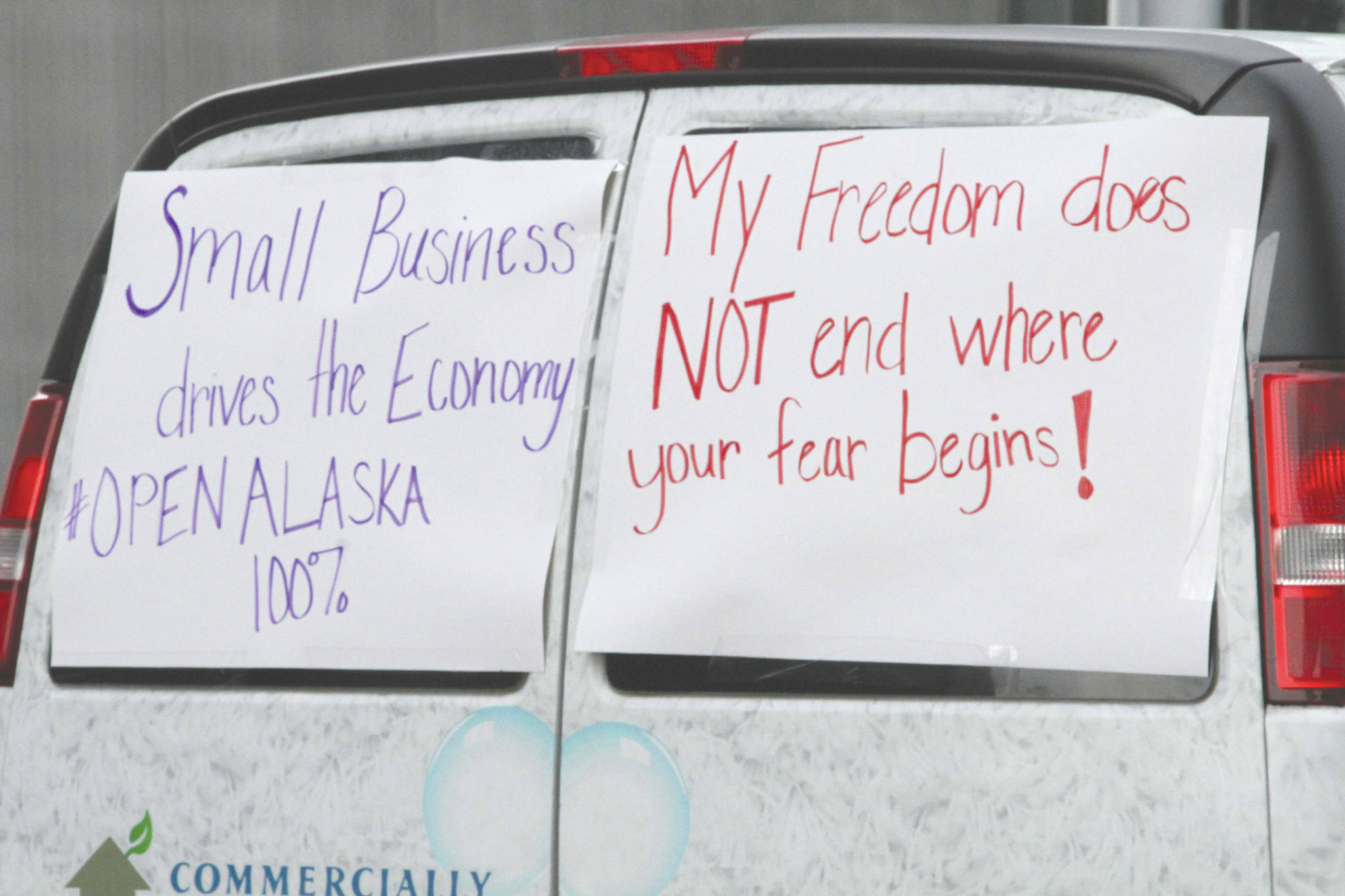 A commercial van with signs on its back windows is driven through downtown Anchorage, Alaska, Wednesday, as part of a caravan of more than 80 vehicles. Participants urged local and state leaders to open up businesses shuttered temporarily while residents were told to stay home. The state will allow some businesses to open Friday, and the city of Anchorage will allow some Monday. (AP Photo/Mark Thiessen)