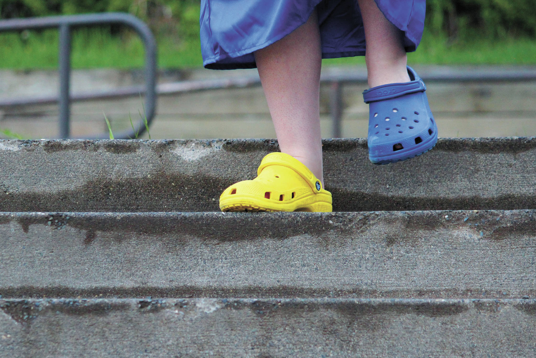 A Homer High School graduate walks down the steps in front of the school wearing Crocs in the Mariner colors after collecting her diploma during the commencement ceremony Monday, May 18, 2020 at the school in Homer, Alaska. (Photo by Megan Pacer/Homer News)