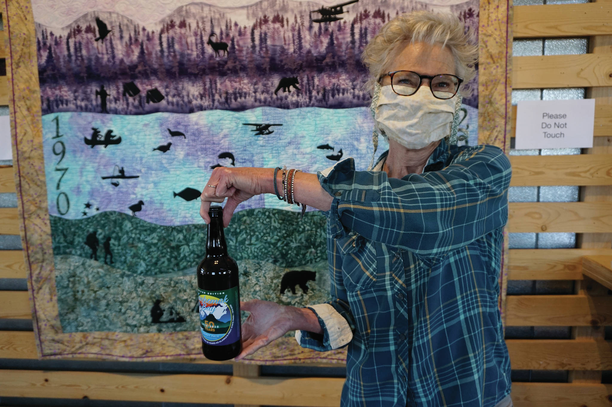 Grace Ridge Brewery co-owner Sherry Stead holds up a bottle of special Kachemak Bay State Park 50th anniversary honey pale ale on Saturday, May 16, 2020, at the brewery in Homer, Alaska. Homer artist Kathy Sarns designed the label. (Photo by Michael Armstrong/Homer News)