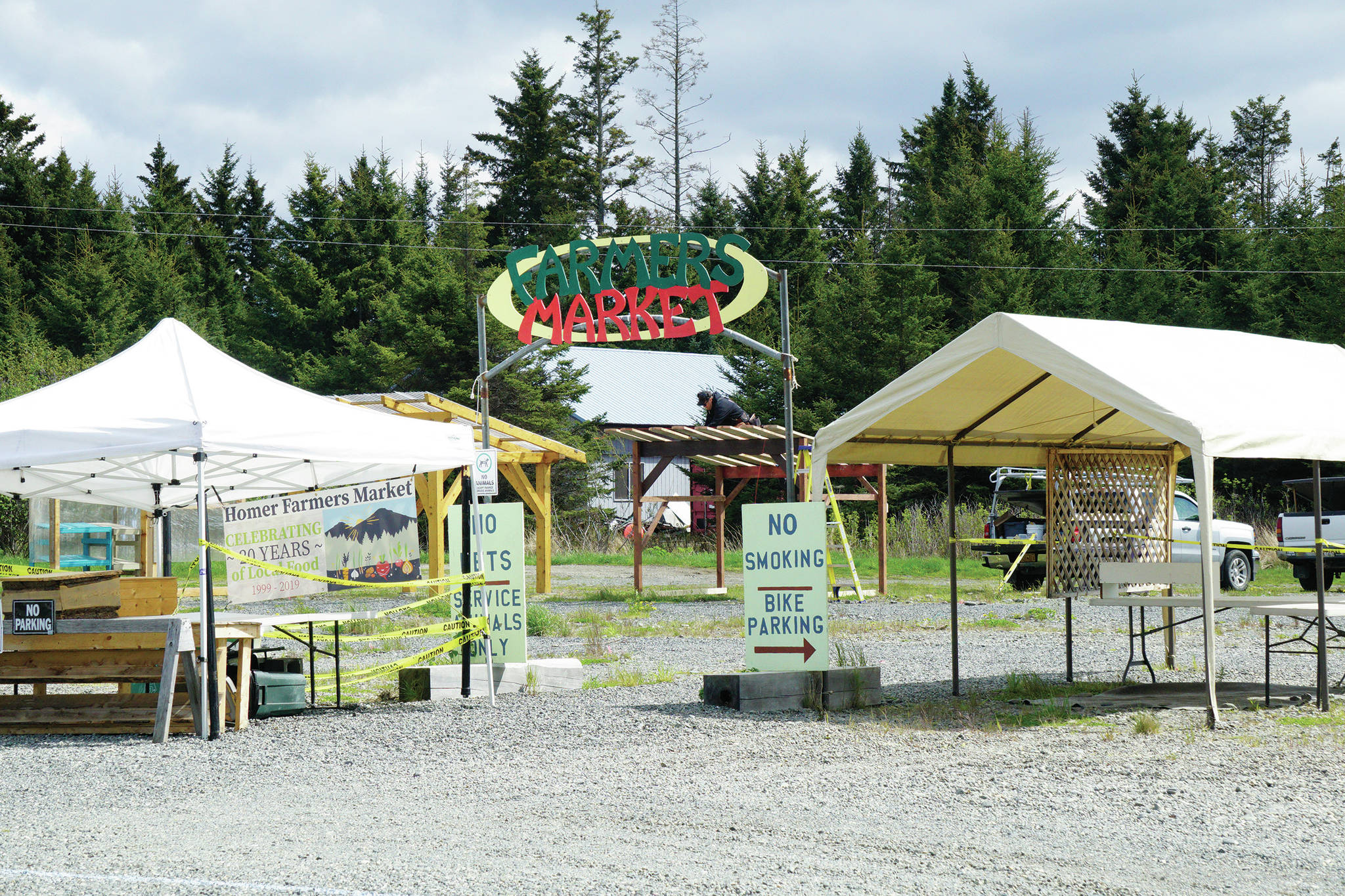 Booths at the Homer Farmers Market stand ready on Monday, May 25, 2020, at the Homer Farmers Market in Homer, Alaska. In the background, Dave Pleznac works on the roof of the Snowshoe Hollow Farm booth while his wife, Christina Castellanos, helps. The market opens on Saturday, May 30, on Ocean Drive in Homer, Alaska. (Photo by Michael Armstrong/Homer News0