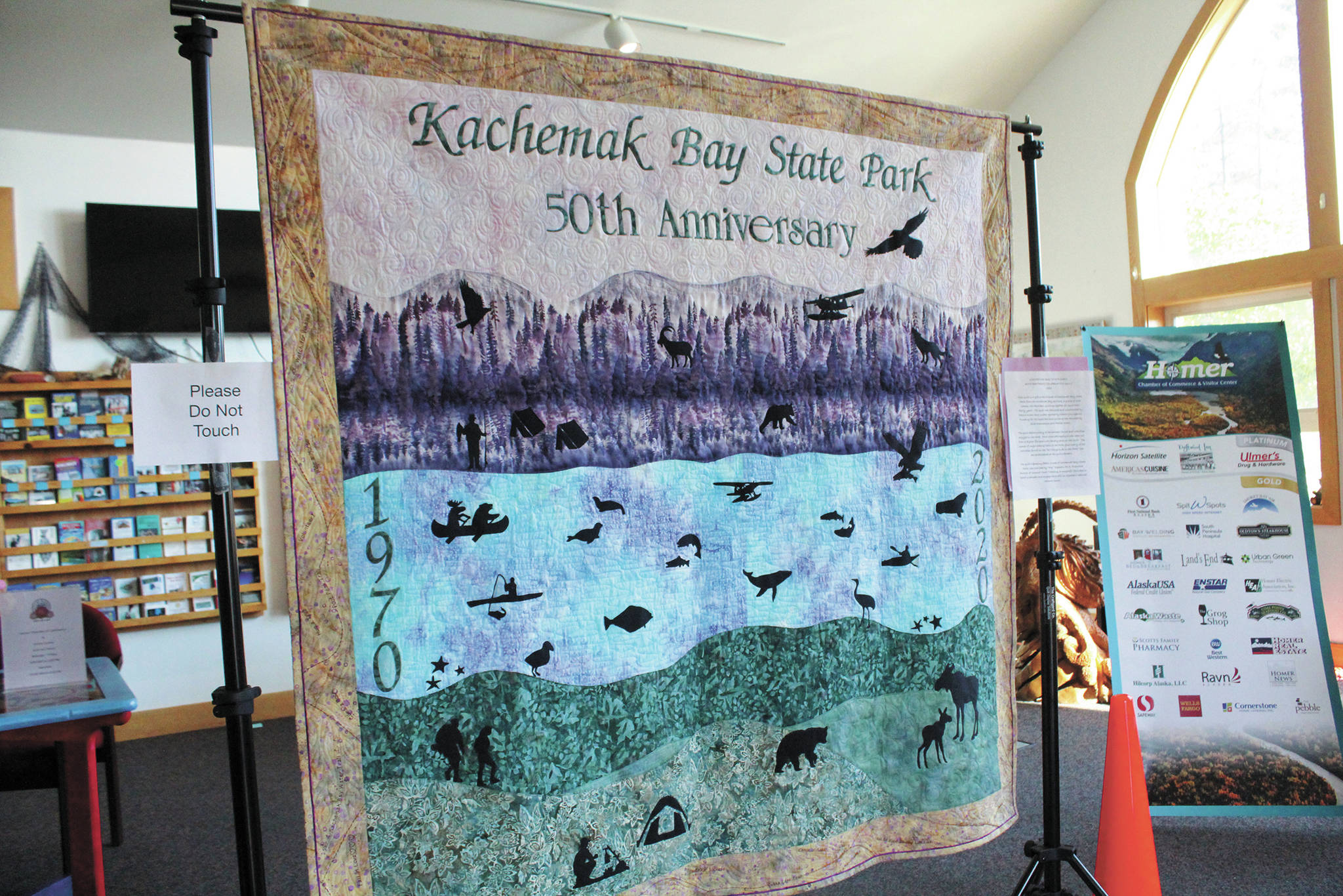 A commemorative quilt made by members of the Kachemak Bay Quilters to celebrate the 50th anniversary of Kachemak Bay State Park hangs in the at the Homer Chamber of Commerce & Visitor Center during a celebration of the park on Saturday, June 6, 2020 in Homer, Alaska. (Photo by Megan Pacer/Homer News)