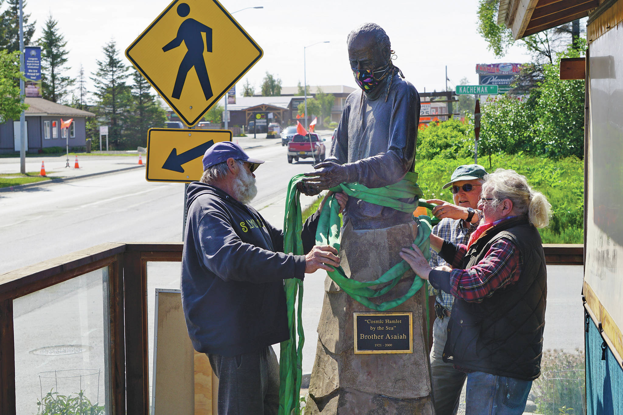 Mike Kennedy, left, Will Files, center, and Leo Vait, right, attach strapes to the Brother Asaiah statue on the deck of Cosmic Kitchen on Saturday, June 6, 2020, in Homer, Alaska. Vait created the statue as a commission by John Nazarian, a friend of Asaiah Bates. Nazarian had loaned to the Pioneer Avenue restaurant the statue of the man who coined the phrase “Cosmic Hamlet by the Sea” to describe Homer. The statue was moved after Cosmic Kitchen owners Michelle Wilson and Sean Hogan sold their restaurant. Cosmic Kitchen closed on Saturday. The Asaiah statue will be stored until a new location can be found. (Photo by Michael Armstrong/Homer News)