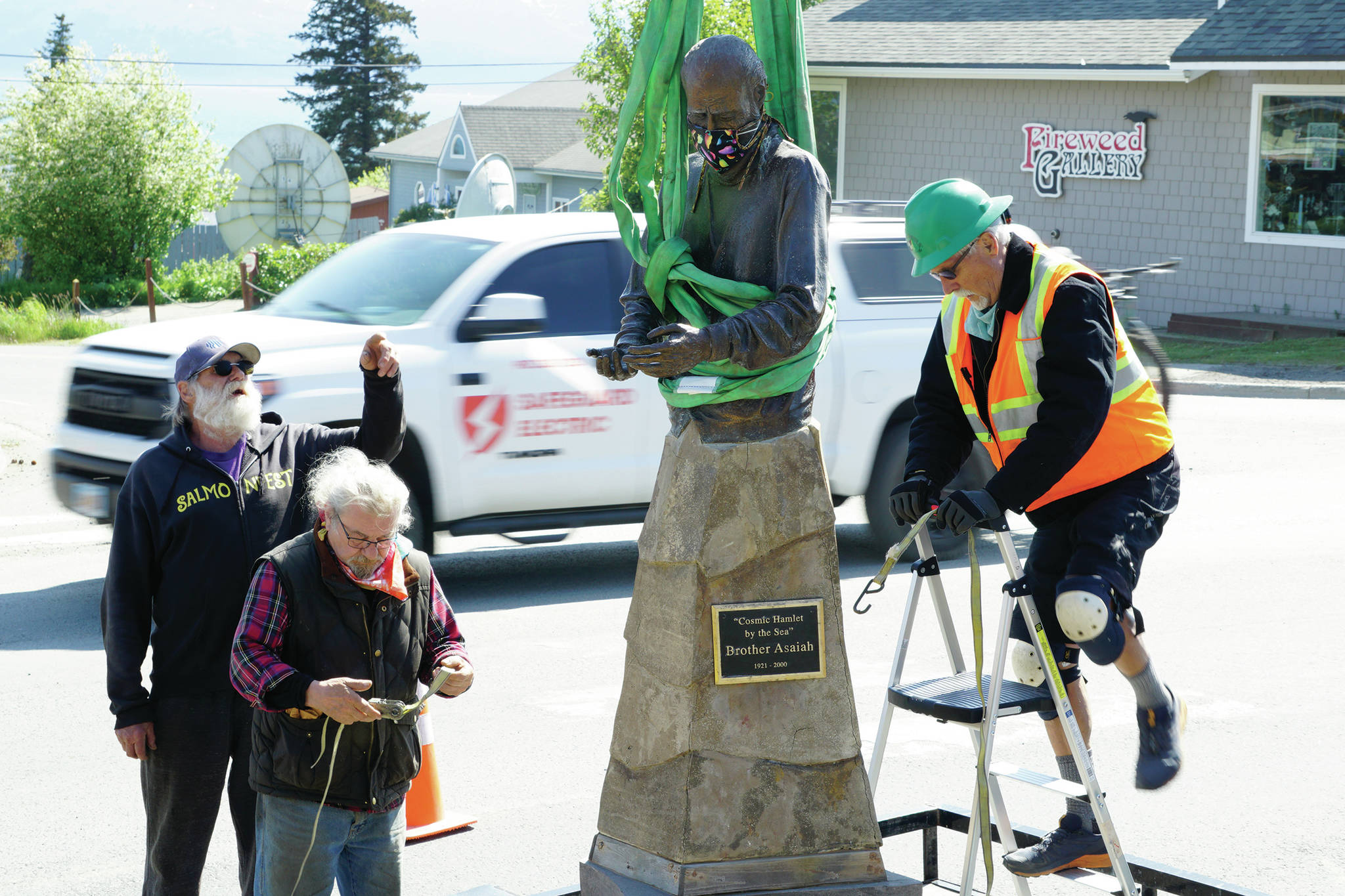 Mike Kennedy, left, Leo Vait, center, and Wayne Aderhold, right, strap the Brother Asaiah statue on a trailer after it was moved from the deck of Cosmic Kitchen on Saturday, June 6, 2020, in Homer, Alaska. Vait created the statue as a commission by John Nazarian, a friend of Asaiah Bates. Nazarian had loaned to the Pioneer Avenue restaurant the statue of the man who coined the phrase “Cosmic Hamlet by the Sea” to describe Homer. The statue was moved after Cosmic Kitchen owners Michelle Wilson and Sean Hogan sold their restaurant. Cosmic Kitchen closed on Saturday. The Asaiah statue will be stored until a new location can be found. (Photo by Michael Armstrong/Homer News)