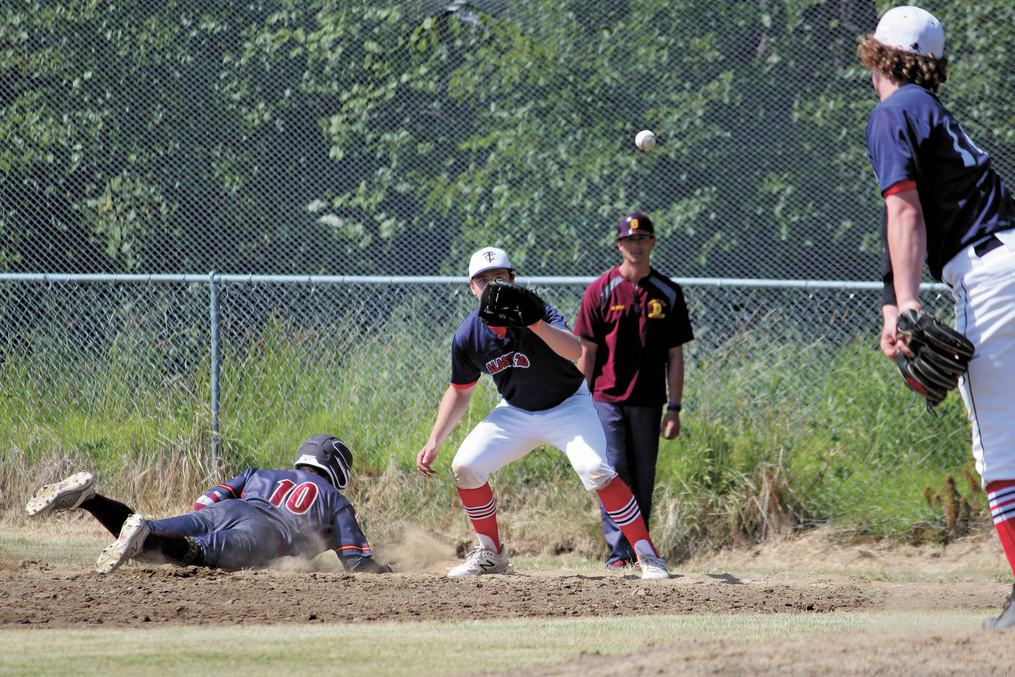 Alaska 20 pitcher Mose Hayes throws the ball to teammate Tanner Ussing while Dimond player Logan Sweet dives back onto first base during a Saturday, July 4, 2020 Alliance Baseball League game at Karen Hornaday Park in Homer, Alaska. (Photo by Megan Pacer/Homer News)