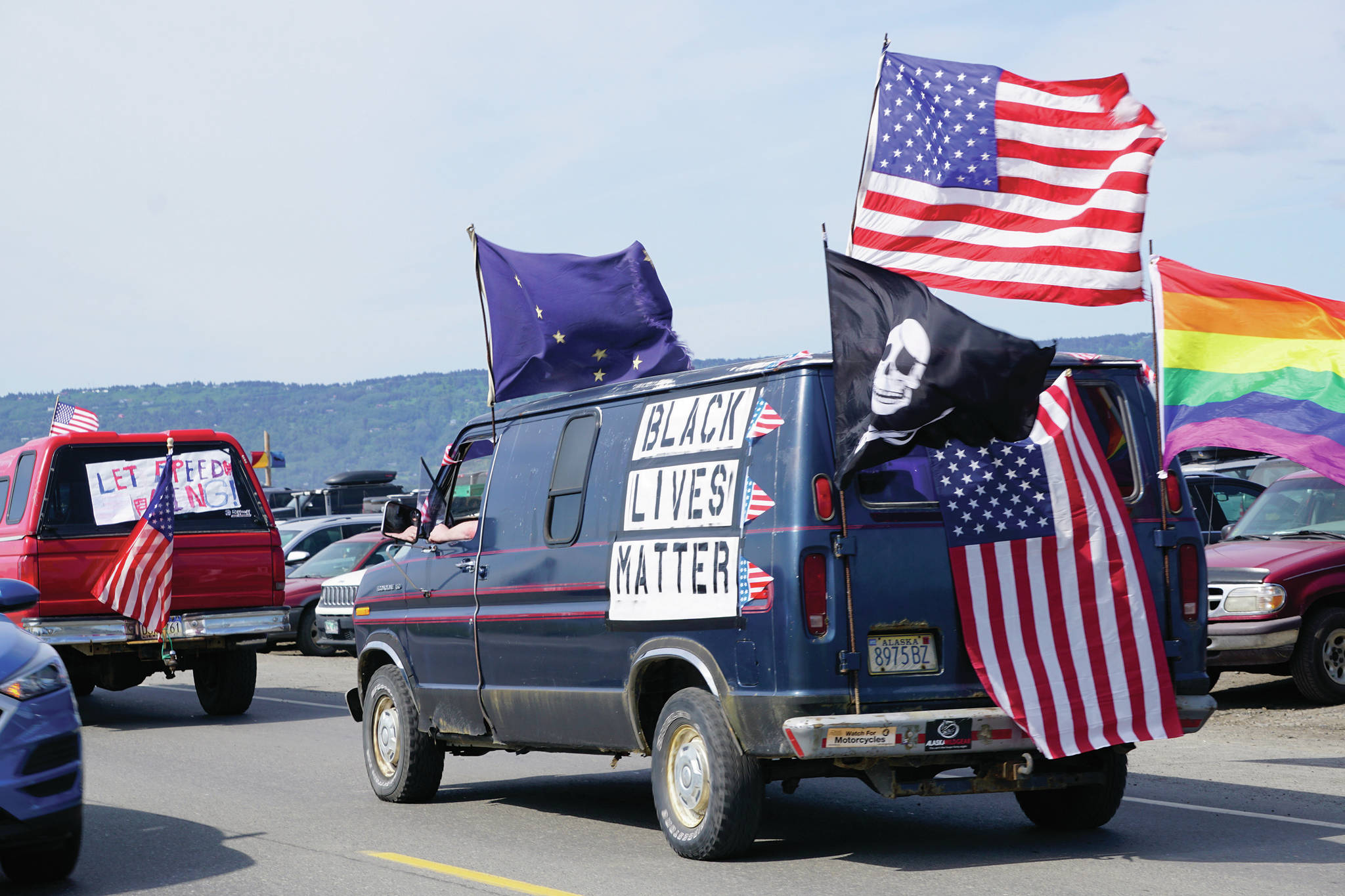 Chris Fischer and Joey Lothian ride in a van with a “Black Lives Matter” banner and U.S., Alaska and Pride flags — and a pirate flag on Saturday, July 4, 2020 in Homer, Alaska. They participated in an unofficial July 4 parade that went from Soundview Avenue on the Sterling Highway to the end of the Homer Spit. (Photo by Michael Armstrong/Homer News)