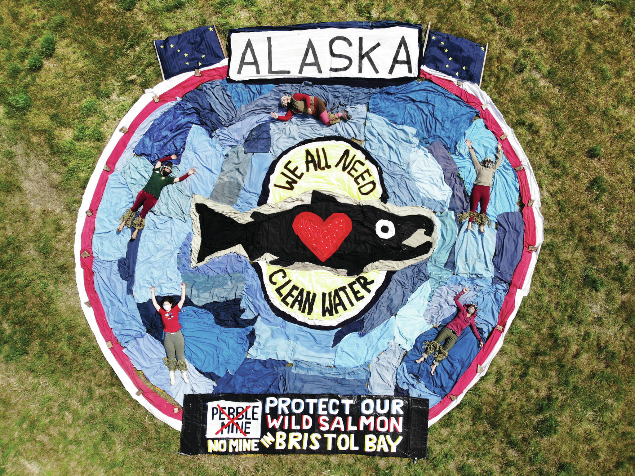 Five artists wearing face masks on Thursday, July 23, 2020, create the annual Salmonfest aerial art in organizing artist Mavis Muller’s field in Homer, Alaska. With used fabric, the group created a ground design “to send a message for the protection of Alaska’s wild salmon, the water they thrive in and the fisheries of Bristol Bay,” said Muller. (Photo by Vernon Ray Pelkey)