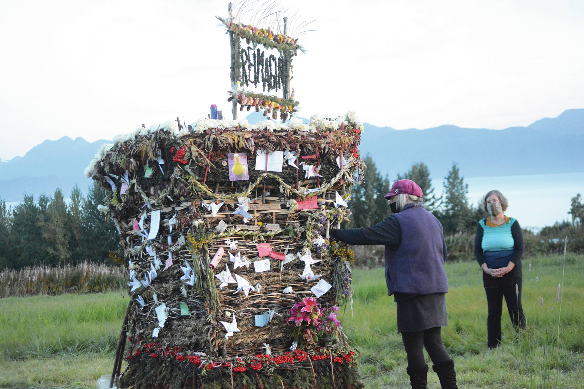 As Peggy Paver right, watches, Mavis Muller, left, places a note in”Reimagine,” the 17th annual Burning Basket, in a field on Sunday, Sept. 13, near Homer. Artist and coordinator Muller intended to broadcast live on Facebook and YouTube the burning of the basket, but because of technical difficulties that didn’t happen. “Burning Basket teaches how to let go of expectations and accept the present moment,” Muller wrote in a text message. “Technology is fickle. The basket, however, did exactly what it promised to do. It helod our collective burderns, our memorials, our joys, sadness, fear, and dispersed all of our good intentions in a plume of smoke, sparks and flames.” (Photo by Michael Armstrong/Homer News)