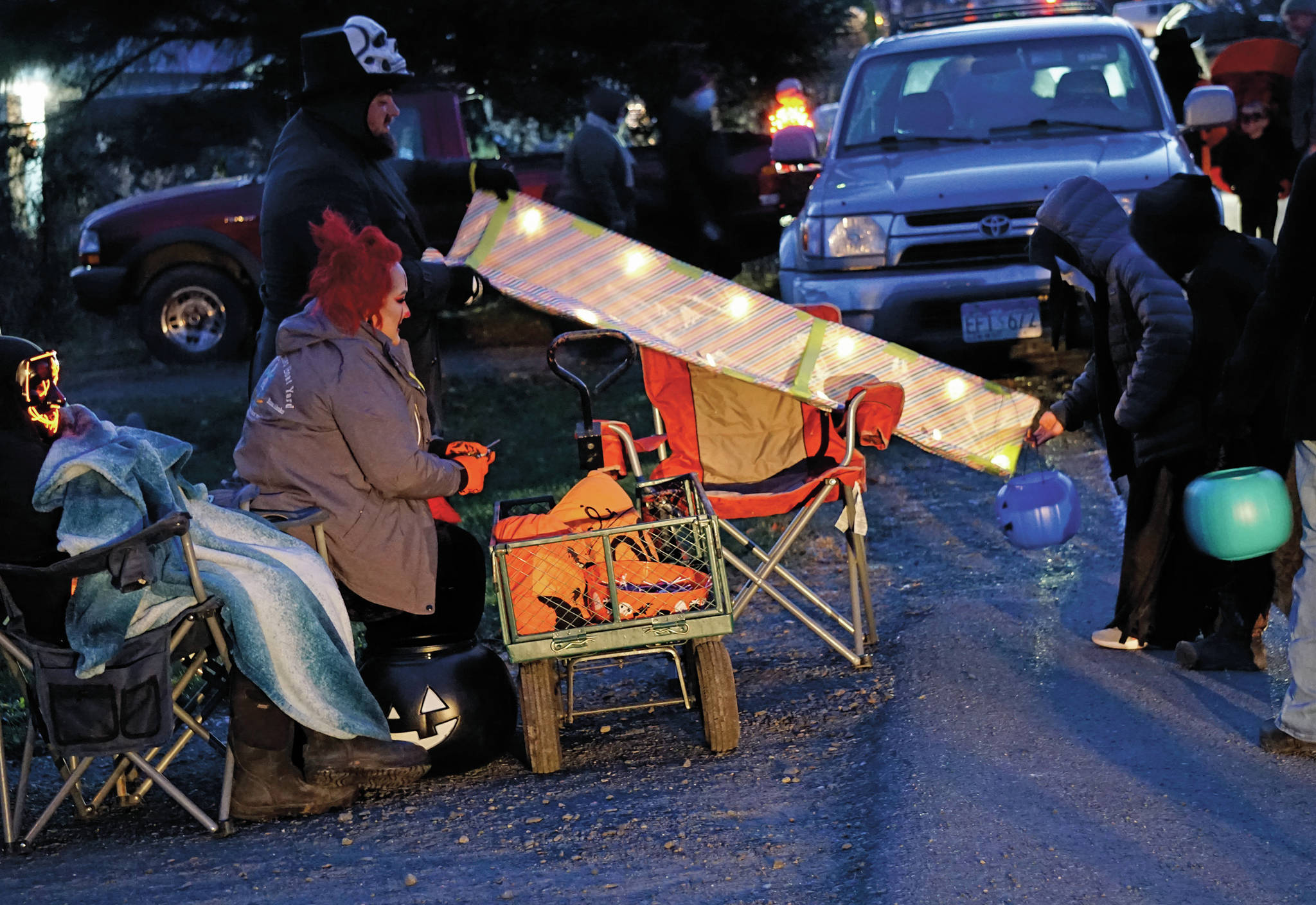 Aaron Fleenor, at top, uses a chute to distribute candy on Halloween night, Oct. 31, 2020, in downtown Homer, Alaska. Helping are Amber Fleenor, center, and Shade Fleenor, left. Because of COVID-19 safety concerns, some people created devices like this to give candy away while keeping social distance. Trick or treating was more subdued than usual, but still drew children in costume to neighborhood above Pioneer Avenue. (Photo by Michael Armstrong/Homer News)