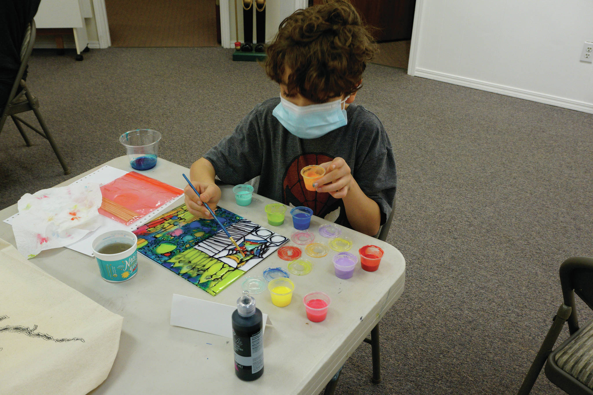 Ryder Chase, age 9, works on faux stained glass in Amy Komar’s socially-distant Art a la Carte class last Friday at the Homer Council on the Arts. Children in the class wore masks and worked at either end of long tables spaced apart. The young artists also made large origami stars that will be placed in store windows “for a dose of color therapy for the community,” Komar said. (Photo by Michael Armstrong/Homer News)