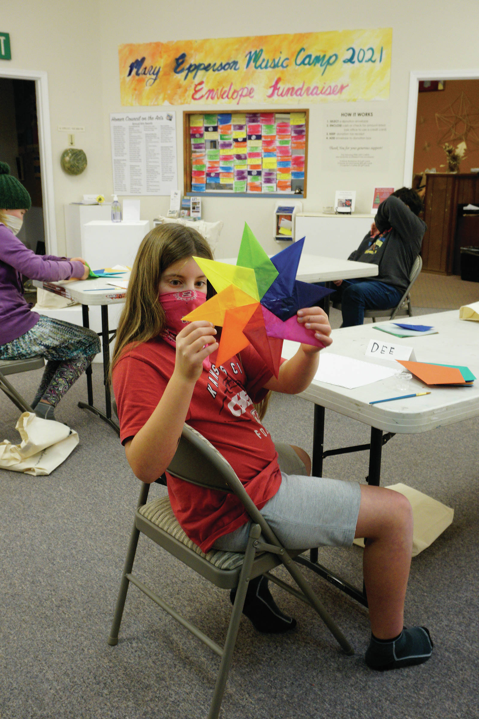 Dee Wilmeth, age 9, shows an origami star she made in Amy Komar’s socially-distant Art a la Carte class last Friday at the Homer Council on the Arts. Children in the class wore masks and worked at either end of long tables spaced apart. The stars will be placed in store windows “for a dose of color therapy for the community,” Komar said. (Photo by Michael Armstrong/Homer News)