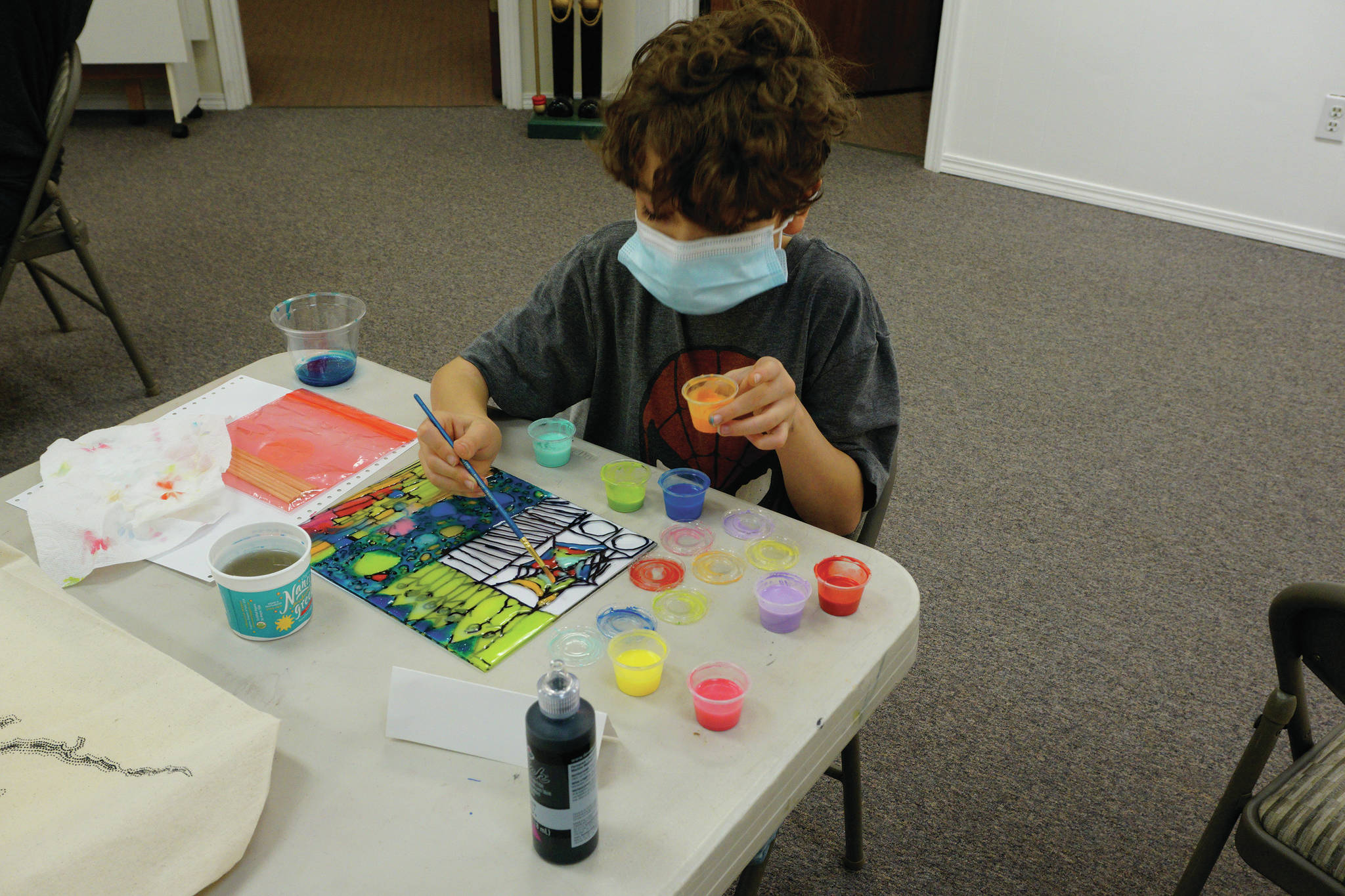 Ryder Chase, age 9, works on faux stained glass in Amy Komar's socially-distant Art a la Carte class last Friday at the Homer Council on the Arts. Children in the class wore masks and worked at either end of long tables spaced apart. The young artists also made large origami stars that will be placed in store windows "for a dose of color therapy for the community," Komar said. (Photo by Michael Armstrong/Homer News)