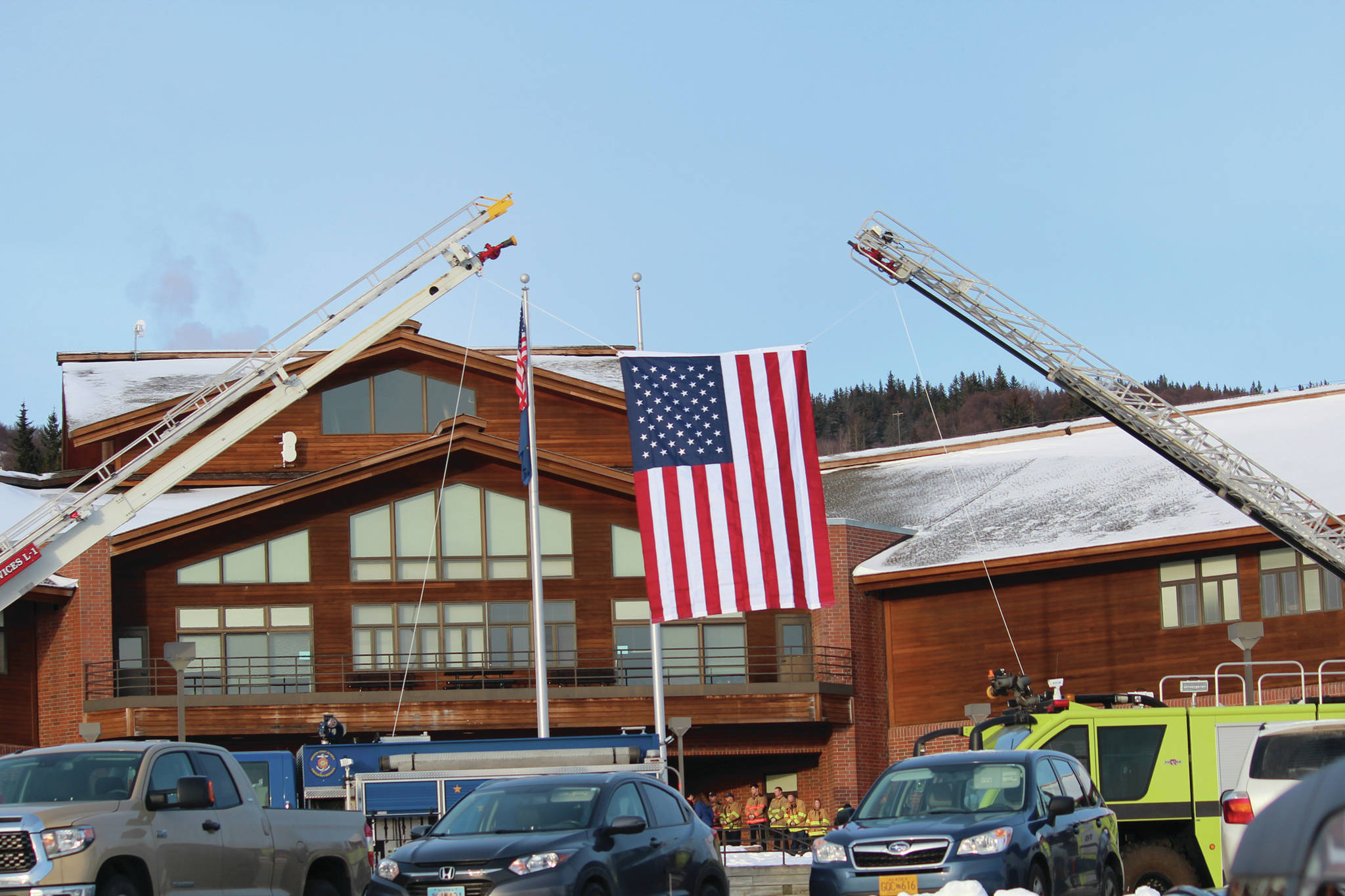 An American flag is suspended between two ladder trucks outside Homer High School for the memorial for Gary Thomas, a Homer man who was killed in a water heater explosion this month, on Sunday, Jan. 19, 2020 in Homer, Alaska. Thomas was a volunteer firefighter for more than 40 years. (Photo by Megan Pacer/Homer News)