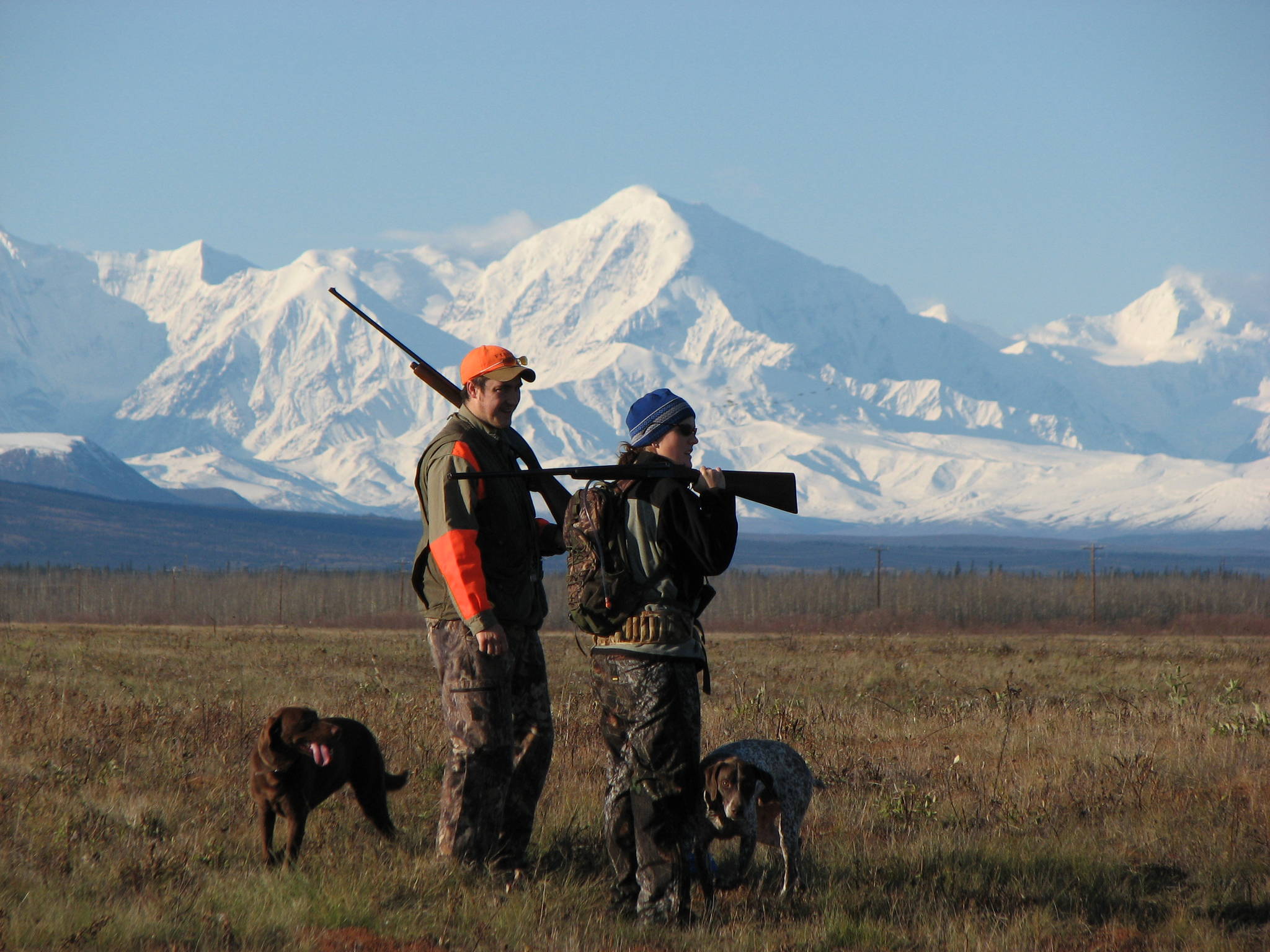 Dwarfed by the majestic and formidable Alaska Range, Michelle and Reed Quinton hunt sharptailed grouse with their dogs Bristol and Sage. (Photo courtesy Mike Chihuly)