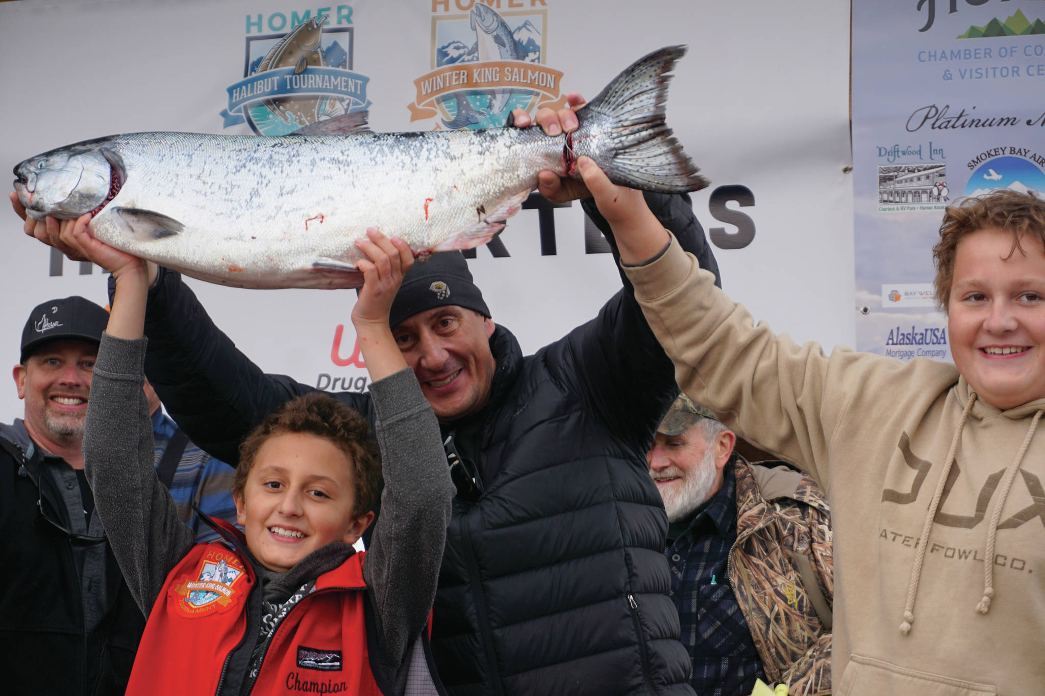 Andrew Marley, the 2021 Homer Winter King Salmon Tournament winner, at left, holds his prize winning 25.62-pound white king salmon on Saturday, April 17, 2021, on the Homer Spit in Homer, Alaska. Helping him are his father, Jay Marley, center, and older brother Weston Marley, right. The family team included Erica Marley, not shown, all fishing on the Fly Dough. (Photo by Michael Armstrong/Homer News)