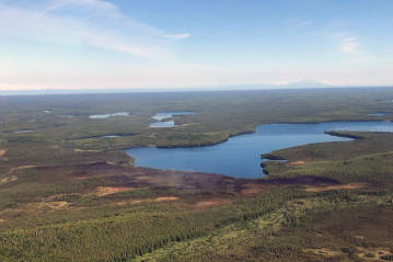 This photo taken at 11:30 a.m. today, Monday, June 14, reveals little smoke rising from the Loon Lake Fire following Sunday’s aerial attack by water and retardant bombing aircraft. The fire denoted by the burned area at the edge of the lake. (Jason Jordet/Division of Forestry Air Attack)