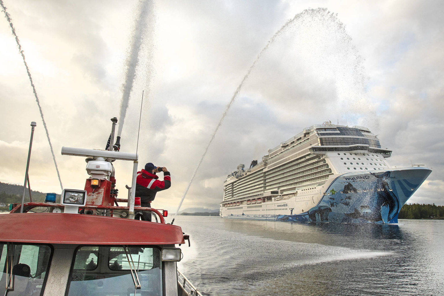 Firefighter medic Andy Tighe snaps a photo of the breakaway plus-class cruise ship Norwegian Bliss while Captain Tracy Mettler operates a fireboat in the Tongass Narrows in Ketchikan, Alaska, on June 4, 2018. President Joe Biden signed into law Monday, May 24, 2021, legislation that opens a door for resumed cruise ship travel to Alaska after the pandemic last year scrapped sailings. (Dustin Safranek / Ketchikan Daily News)