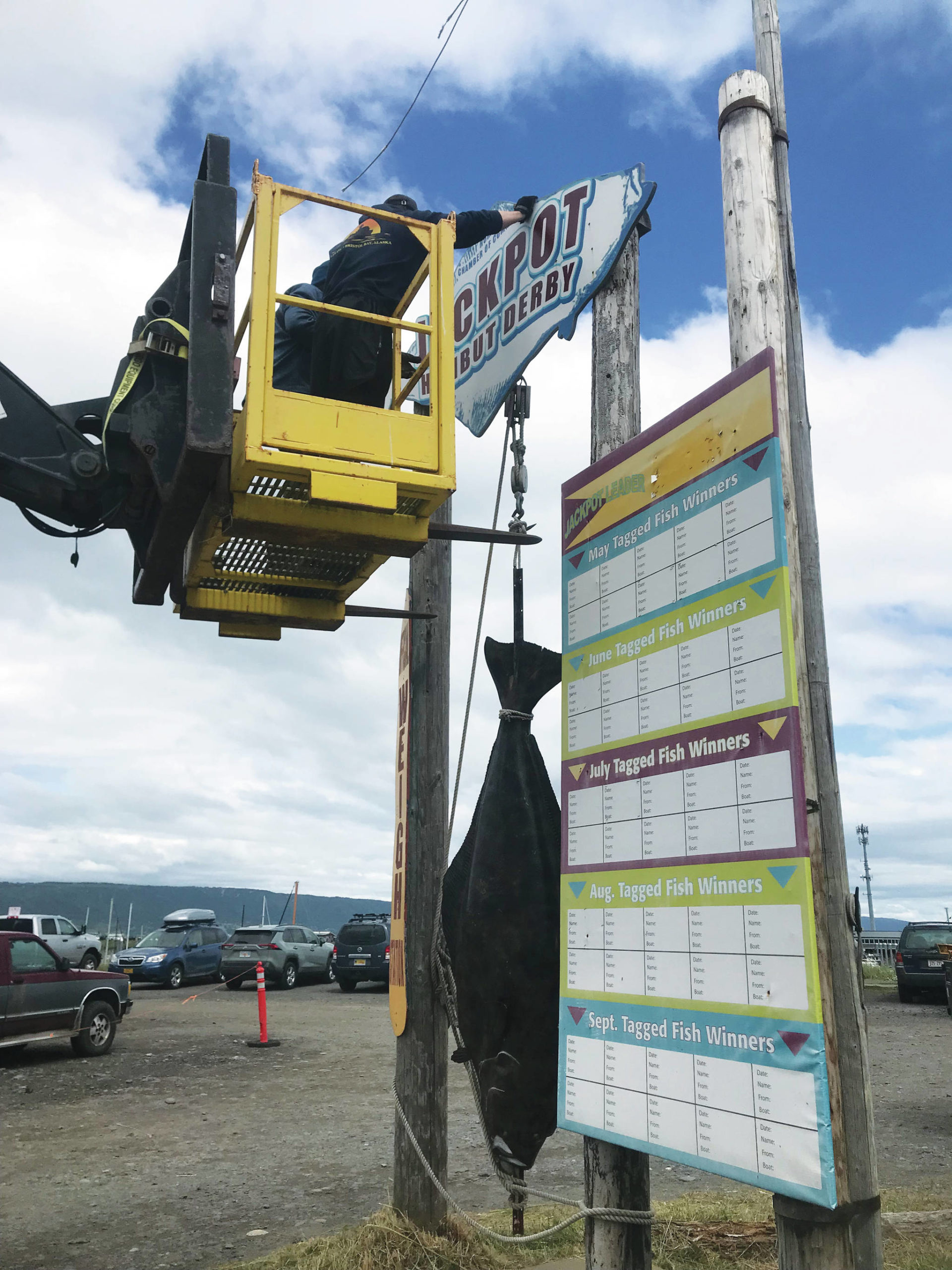 Harbor employees on Friday, July 25, 2021, remove the Jackpot Halibut Derby sign at the former derby shack in Homer, Alaska. The sign will be repainted by Homer artist Dan Coe. (Photo by Christina Whiting)