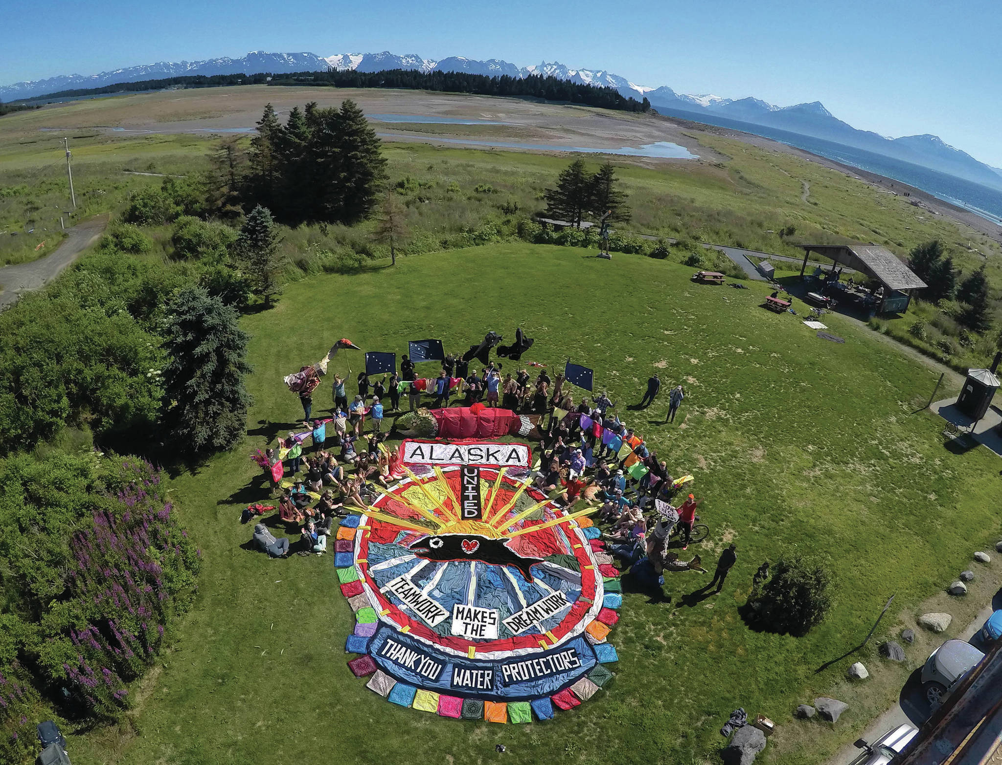 Homer’s Bishop’s Beach Park was the location for an enactment of public participatory art on Sunday, Aug. 1, 2021, in Homer, Alaska. A ground design of colored fabric was created to convey a message of “Alaska United,” “Teamwork Makes the Dream Work” and “Thank You Water Protectors.” The public was invited to be part of the art by standing and sitting around the central design. Salmon sculptures, raven and sandhill crane puppets, Alaska flags and colored bandanas were an added touch to the overhead image depicting salmon solidarity. The project was led by Mavis Muller and was the finale to her series of 12 annual aerial group photos for the protection of Alaska’s Bristol Bay. Photographer Russell Campbell captured the photo from a bucket lift at 35 feet high. “Art is communication. With our creativity and imagination we can inspire new possibilities, and we can have fun doing it,” Muller said. (Photograph by Russell Campbell)
