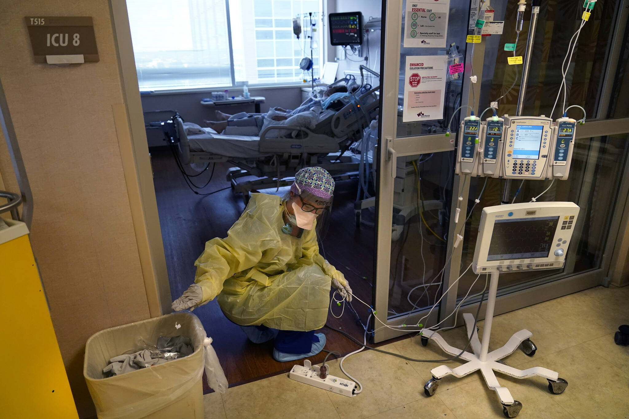 An ICU nurse, moves electrical cords for medical machines, outside the room of a patient suffering from COVID-19, in an intensive care unit at the Willis-Knighton Medical Center in Shreveport, La. The COVID-19 pandemic has created a nurse staffing crisis that is forcing many U.S. hospitals to pay top dollar to get the help they need to handle the crush of patients this summer. (AP Photo/  Gerald Herbert)