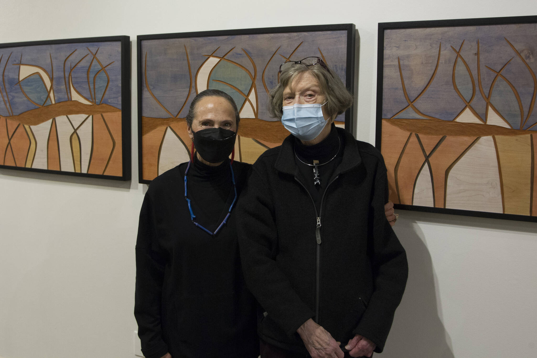 Rika Mouw and Turid Senungetuk, wife of Ron Senungetuk, stand in front of Ron Senungetuk's artworks titled "Reindeer Herd I, II, III" during the exhibit's opening reception at the Pratt Museum and Park. (Photo by Sarah Knapp/Homer News)