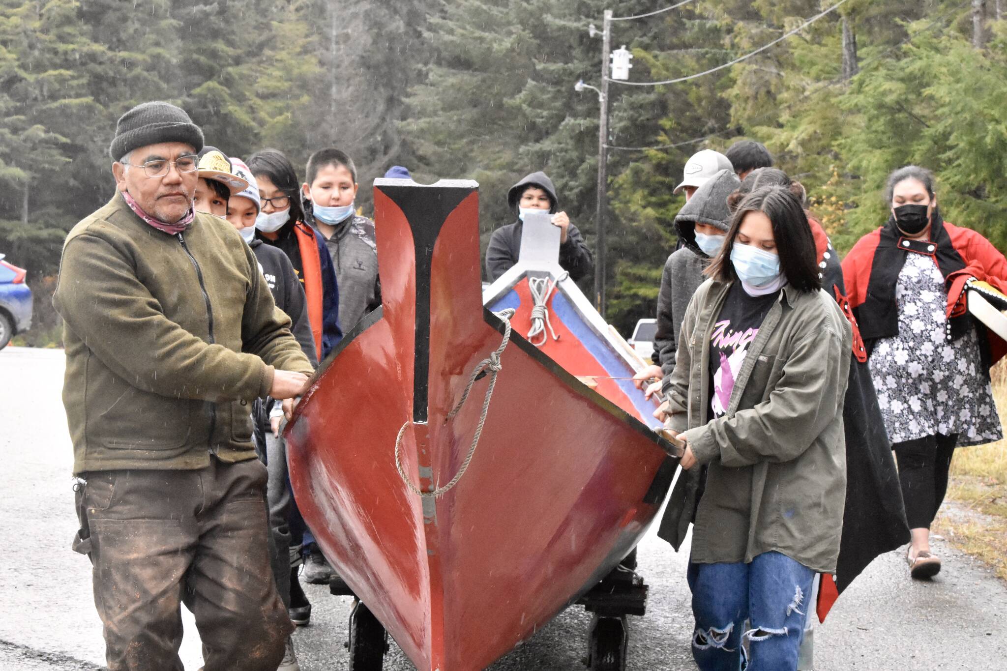 Tlingit master carver Wayne Price, left, and students from Angoon High School wheel a dugout canoe down to the Angoon waterfront on Tuesday, Oct. 26, 2021, for a ceremony commemorating the bombardment of the village by the U.S. Navy in 1882. Dugout canoes were specifically targeted by the navy for destruction, and Price said crafting a new one was a way of healing from the past. (Peter Segall / Juneau Empire)