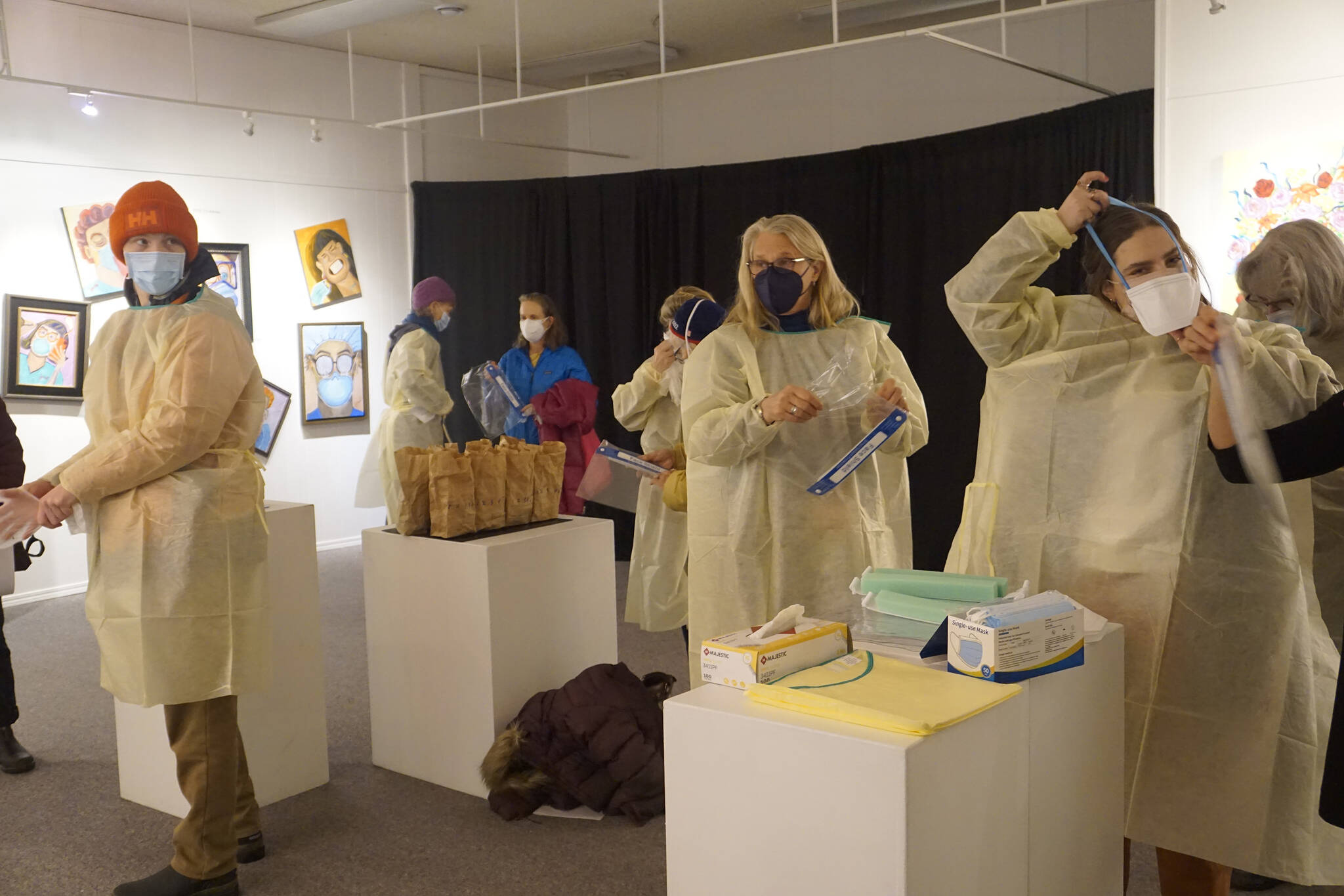 Visitors put on personal protective equipment before an artist talk by Dr. Sami Ali' at the Jan. 7, 2022, First Friday opening of her exhibit, "The Mind of a Healthcare Worker During the COVID-19 Pandemic," at the Homer Council on the Arts in Homer, Alaska. (Photo by Michael Armstrong/Homer News)