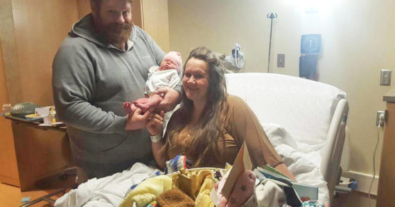 Jacob Fraley, left, holds his new daughter, Betty Lynn Fraley, while mother Cassy Quinlan, right,  watches on Wednesday, Jan. 19, 2022, at South Peninsula Hospital in Homer, Alaska. Betty Lynn was born on Jan. 17, 2022, the first baby of the New Year. Some of the gifts the family received for having the first baby of the year are in front of Quinlan. (Photo courtesy of South Peninsula Hospital)