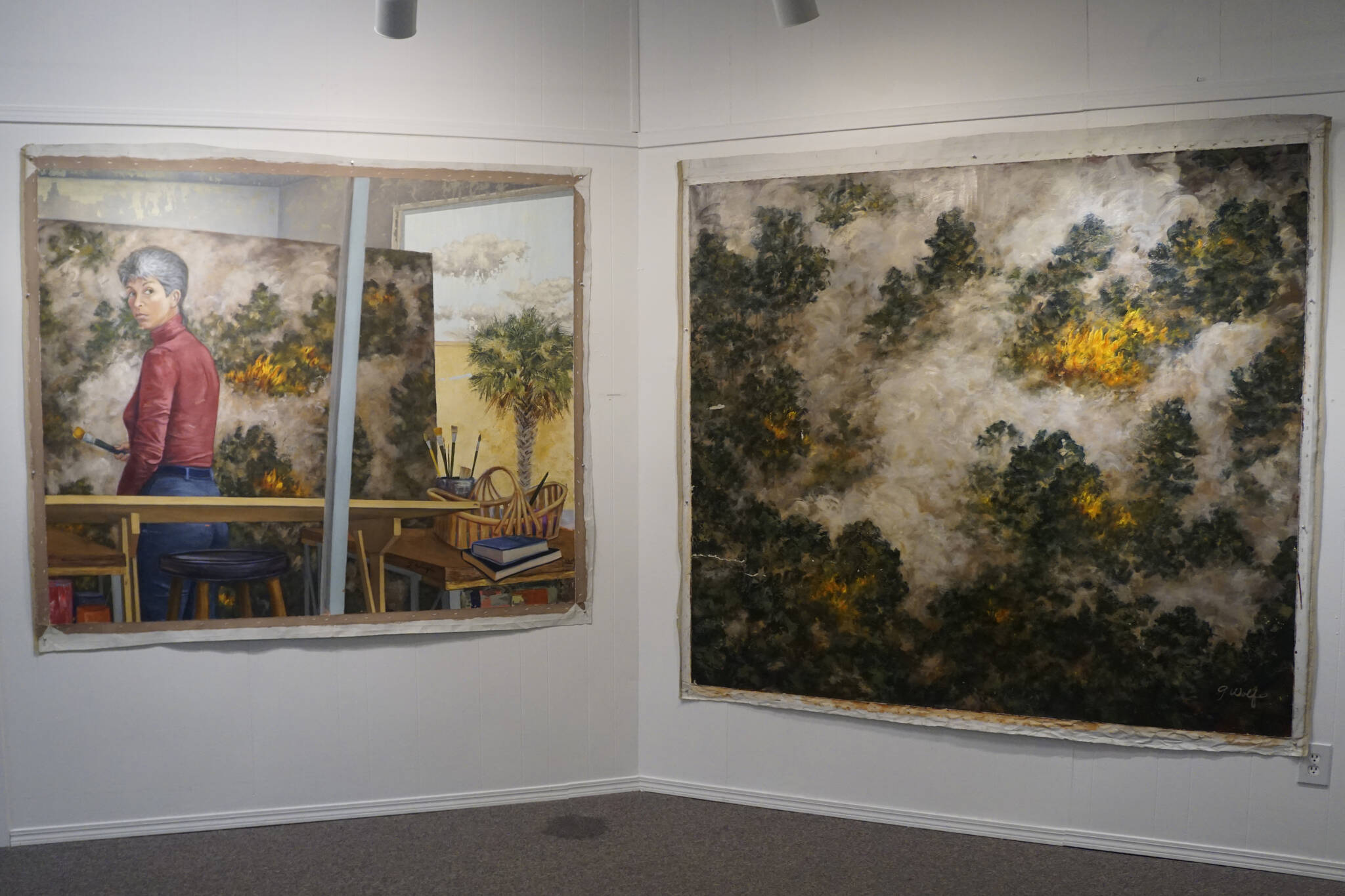 "Selected Works and Sketches by Gaye Wolfe," showing at the Homer Council on the Arts through March, includes these two paintings by Wolfe: a painting of a wildfire, right, and then a self-portrait of Wolfe, left, creating the painting. (Photo by Michael Armstrong/Homer News)