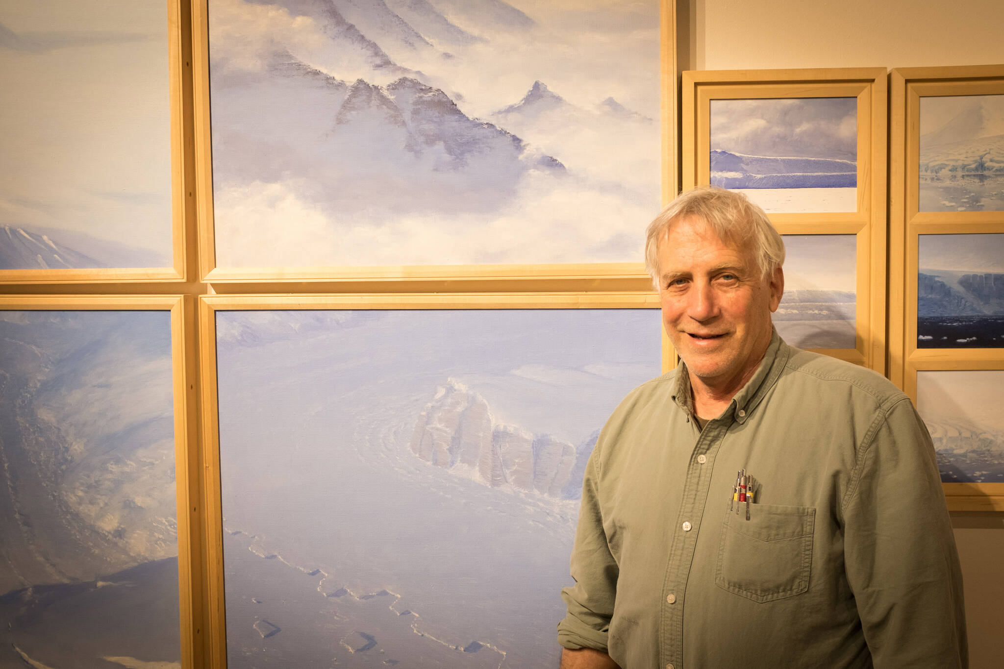 David Rosenthal poses for a portrait in front of paintings from his time in Antarctica at the Pratt Museum & Park in Homer, Alaska. (Photo by Sean McDermott)