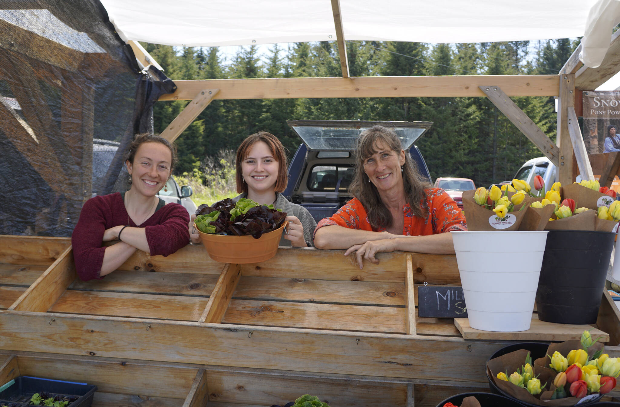 Homer Hilltop Farm workers are all smiles after selling out mixed greens on the first day of the Homer Farmers Market on Saturday, May 28, 2022, in Homer, Alaska. From left to right are Anna Passaniti, Abby Blaize and farm owner Carey Restino. (Photo by Michael Armstrong/Homer News)