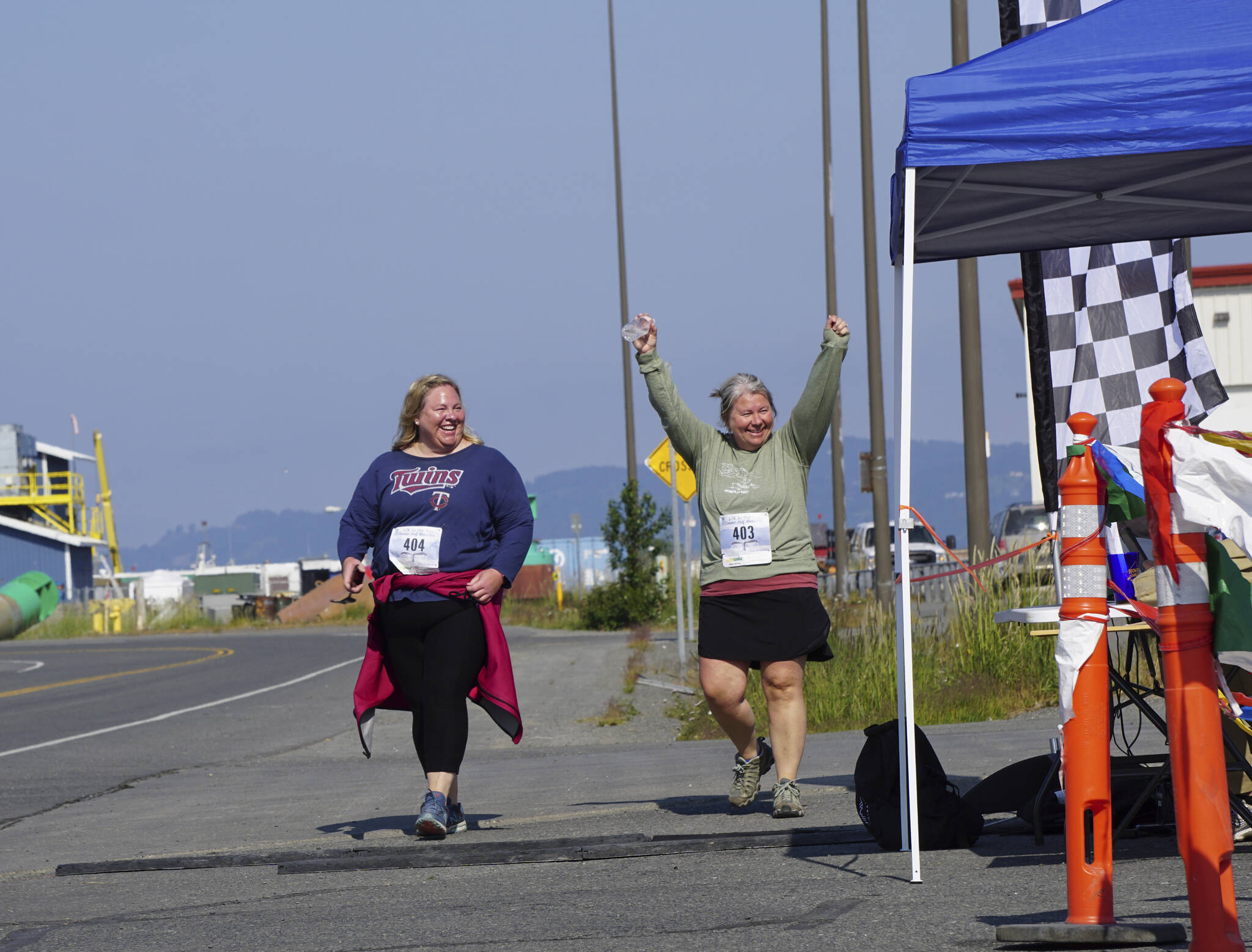 Walkers Jenny Johnson, left, and Jane Nollar, right, cross the finish line in the 2022 Homer Spit Run on Saturday, June 25, 2022, at the End of the Road Park in Homer, Alaska. (Photo by Michael Armstrong/Homer News)