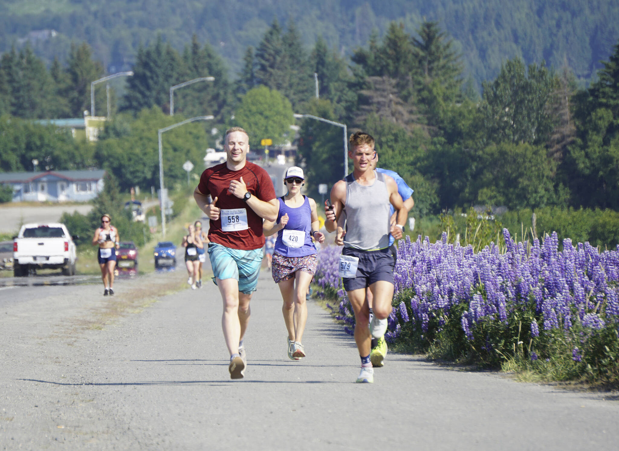 Silas Firth, left, Emily Knight, center, and Craig Albers, right, run past lupines in the 2022 Homer Spit Run 10k and Half Marathon on Saturday, June 25, 2022, in Homer, Alaska. (Photo by Michael Armstrong/Homer News)
