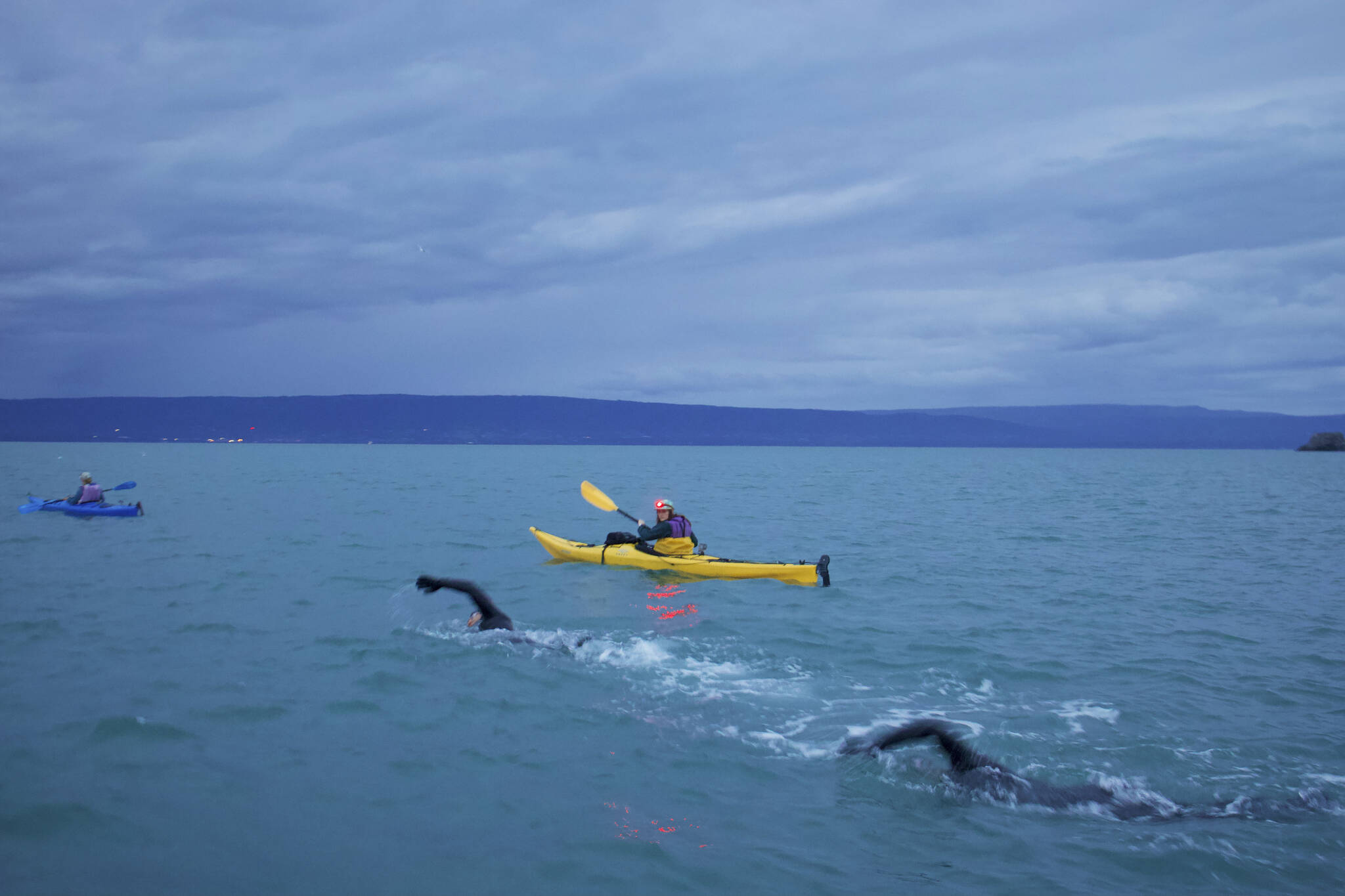 Skyler Rodriquez, left, and Leif Restad, right, swim across Kachemak Bay near Homer, Alaska, on Thursday, Aug. 18, 2022. Kayakers Brita Restad, left, and Autumn Daigle, right, helped guide them. (Photo by Ella Blanton Yourkowski)