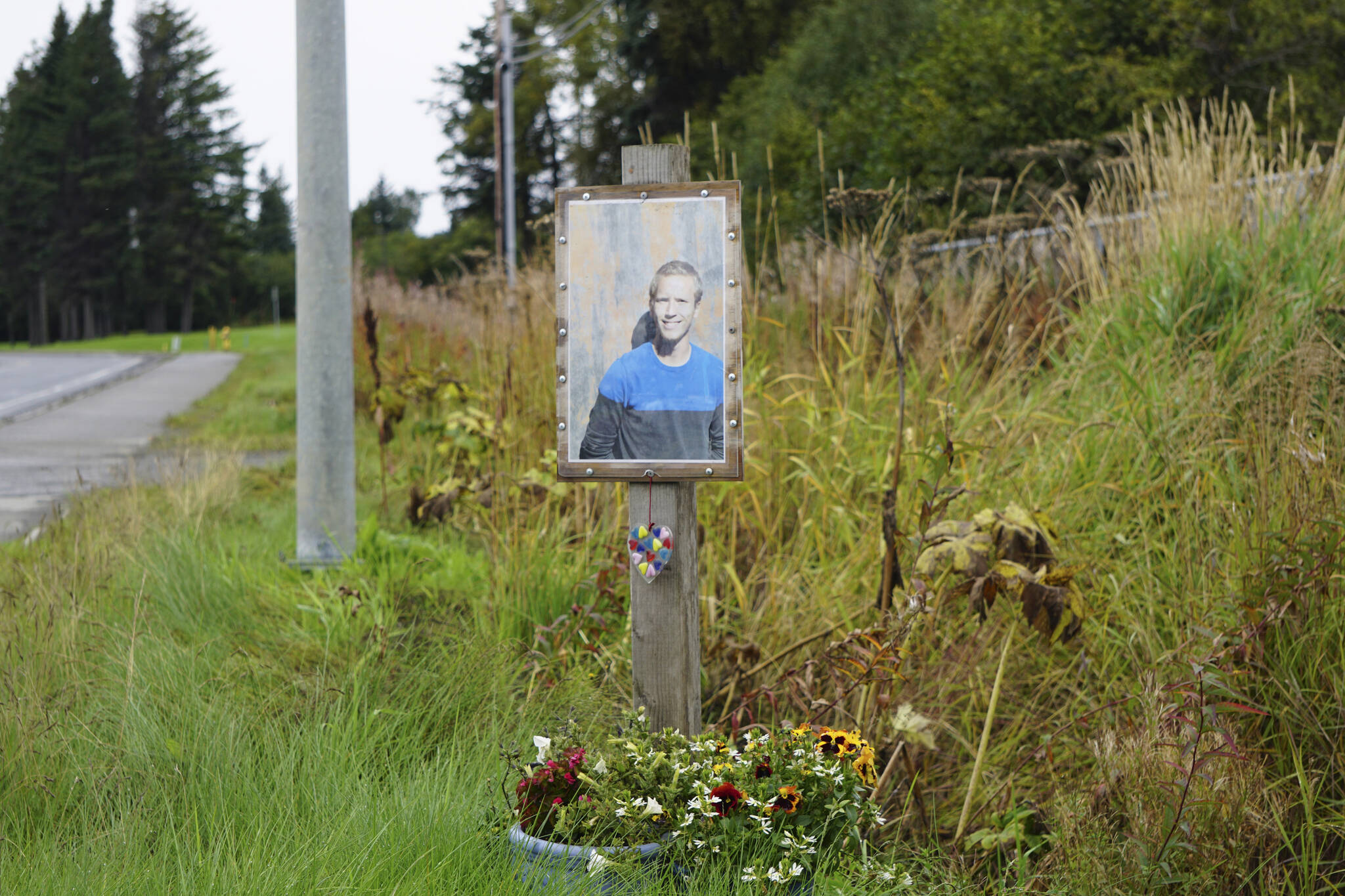 A memorial for Drew Brown with his photo, flowers and a heart sculpture was installed at the site where he died in a car crash on the Sterling Highway, as seen here on Friday, Sept. 16, 2022, in Homer, Alaska. (Photo by Michael Armstrong/Homer News)