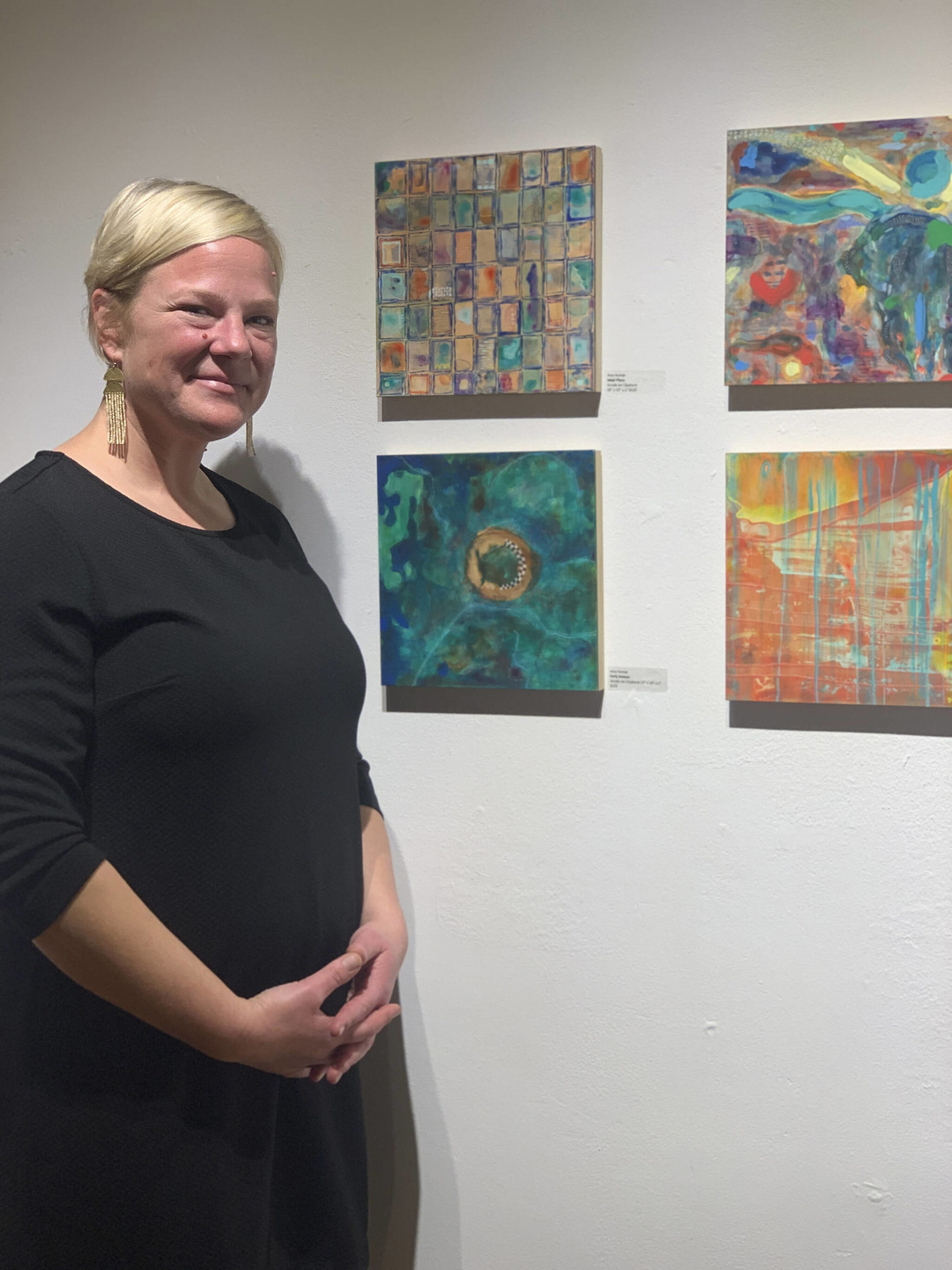 Amy Komar poses with her acrylic on clay board paintings at one the opening of the Mother exhibit showing this month at Bunnell Street Arts Center. (Photo by Christina Whiting)